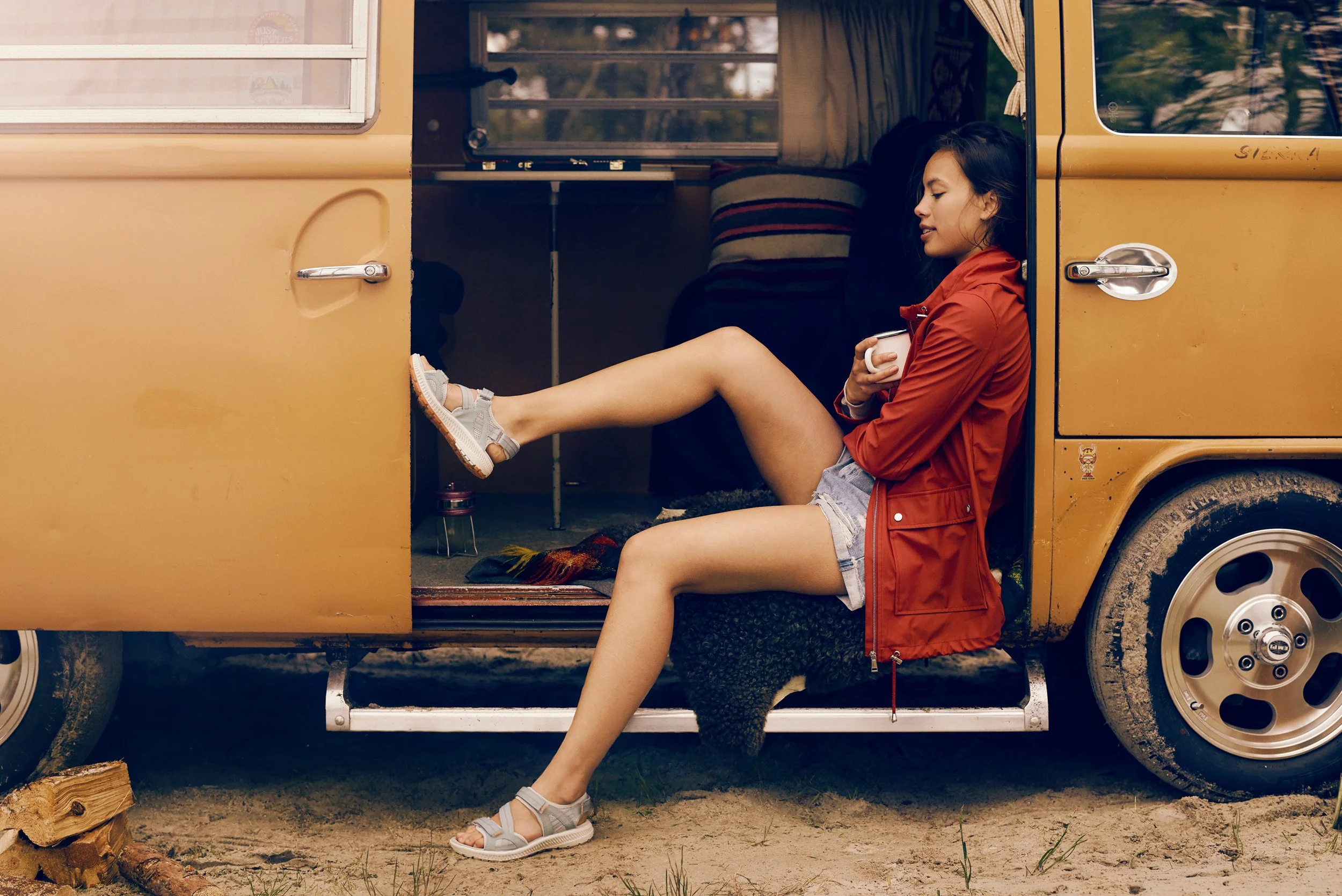 Woman sitting in van doorway holding cup, relaxed outdoor travel moment