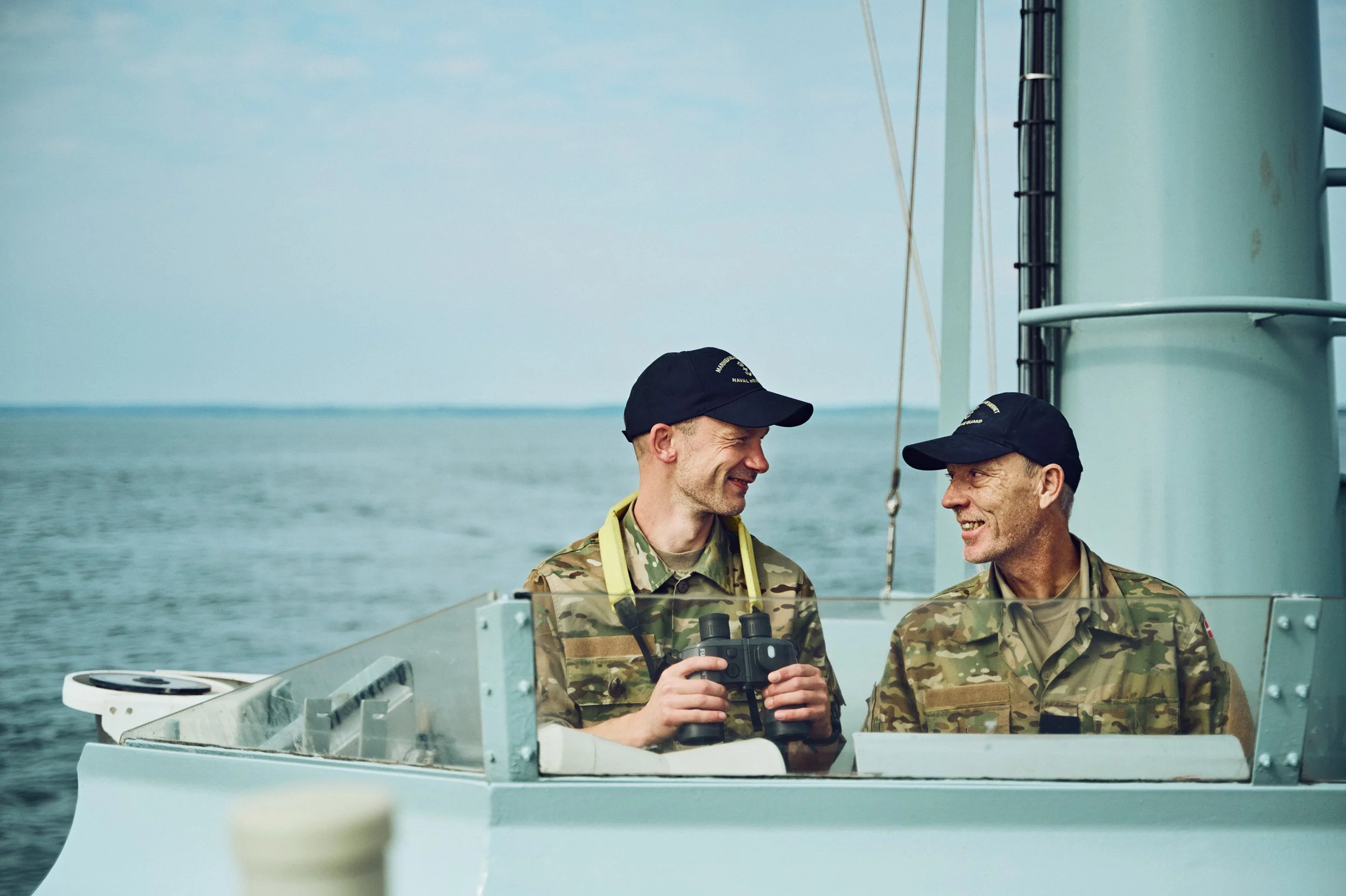 Two Home Guard soldiers standing on ship bridge, communicating and observing surroundings at sea
