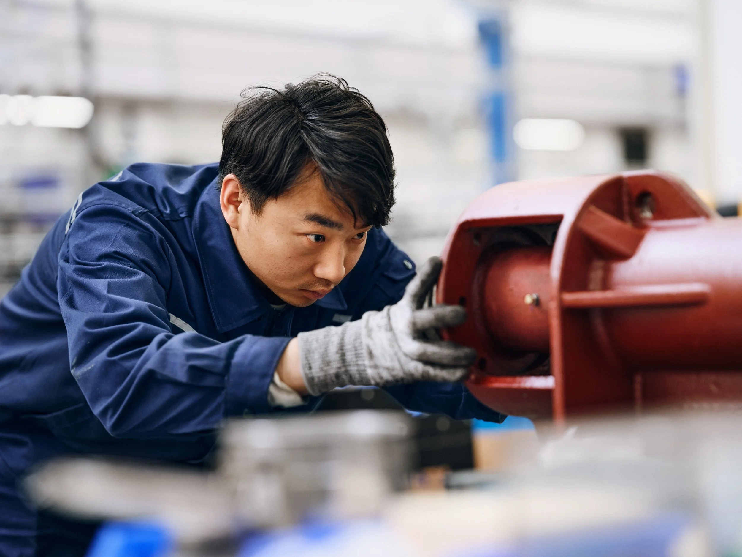 Worker adjusting red pump component in factory, focused close-up during assembly process