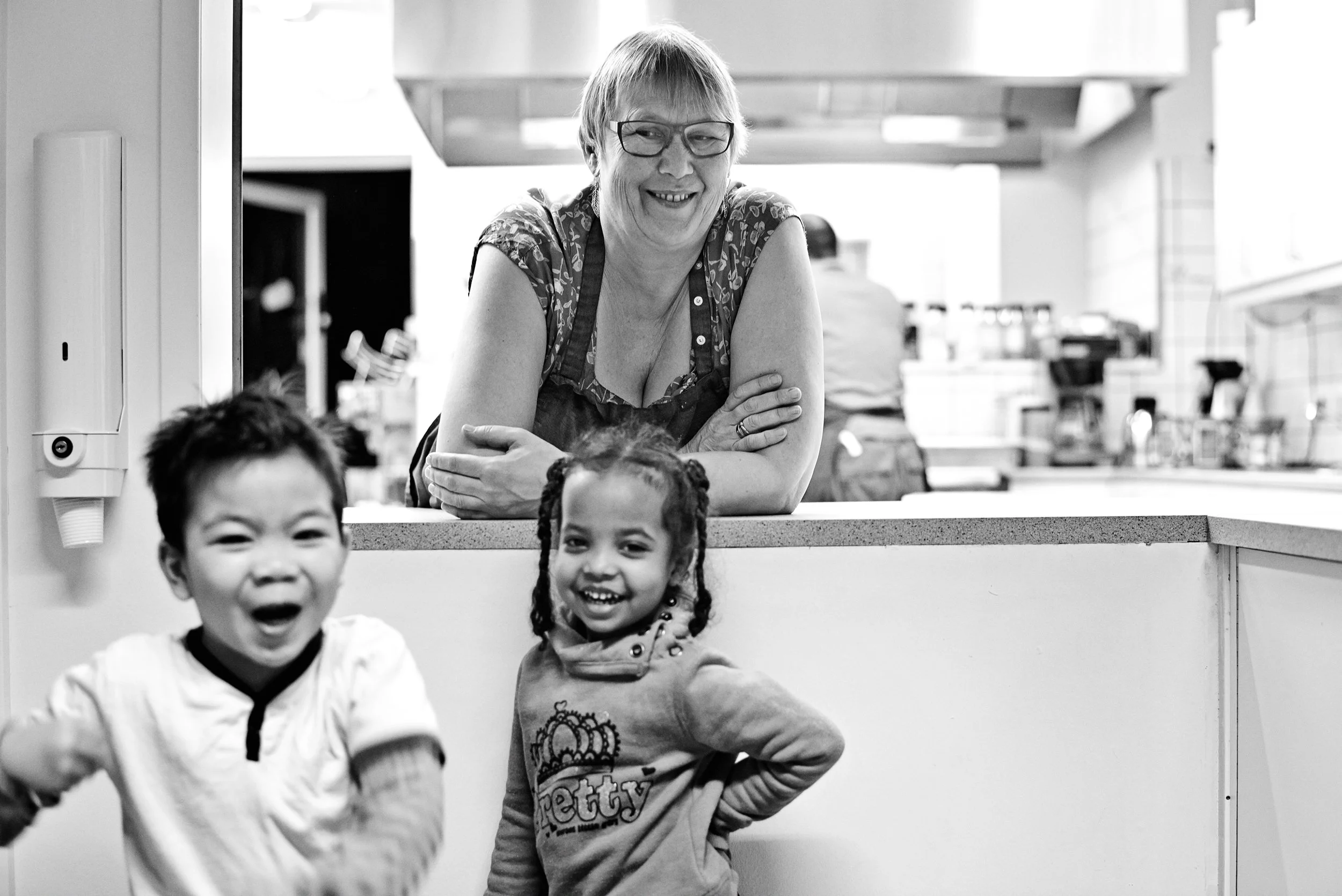 Woman leaning over counter with two children in kitchen, lively everyday moment