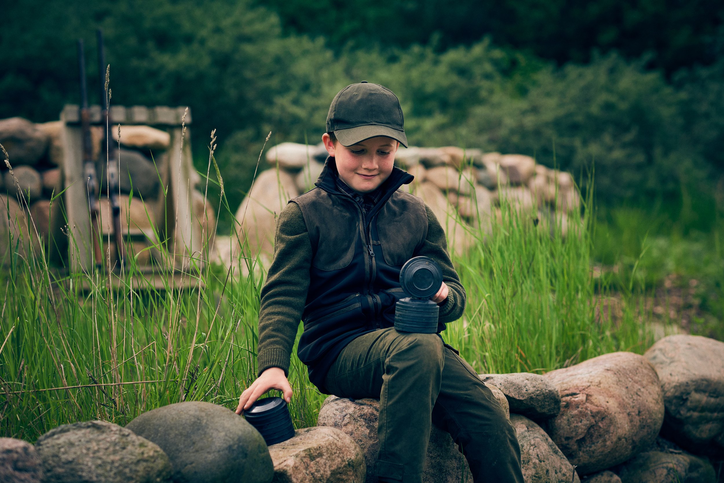 Child sitting on stone wall holding gear, early involvement in outdoor activity