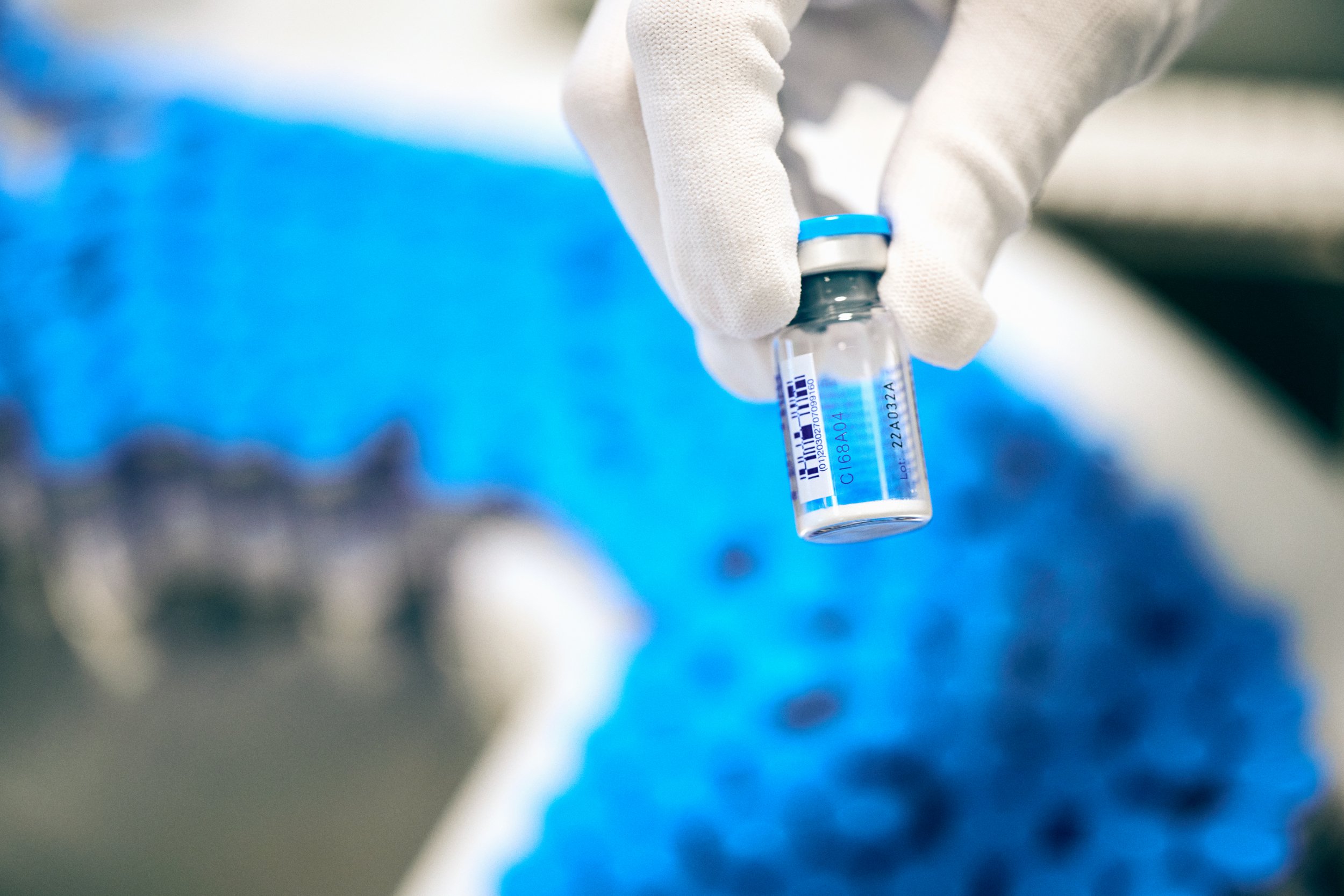 Gloved hand holding sealed vial with liquid, focus on sample handling and containment