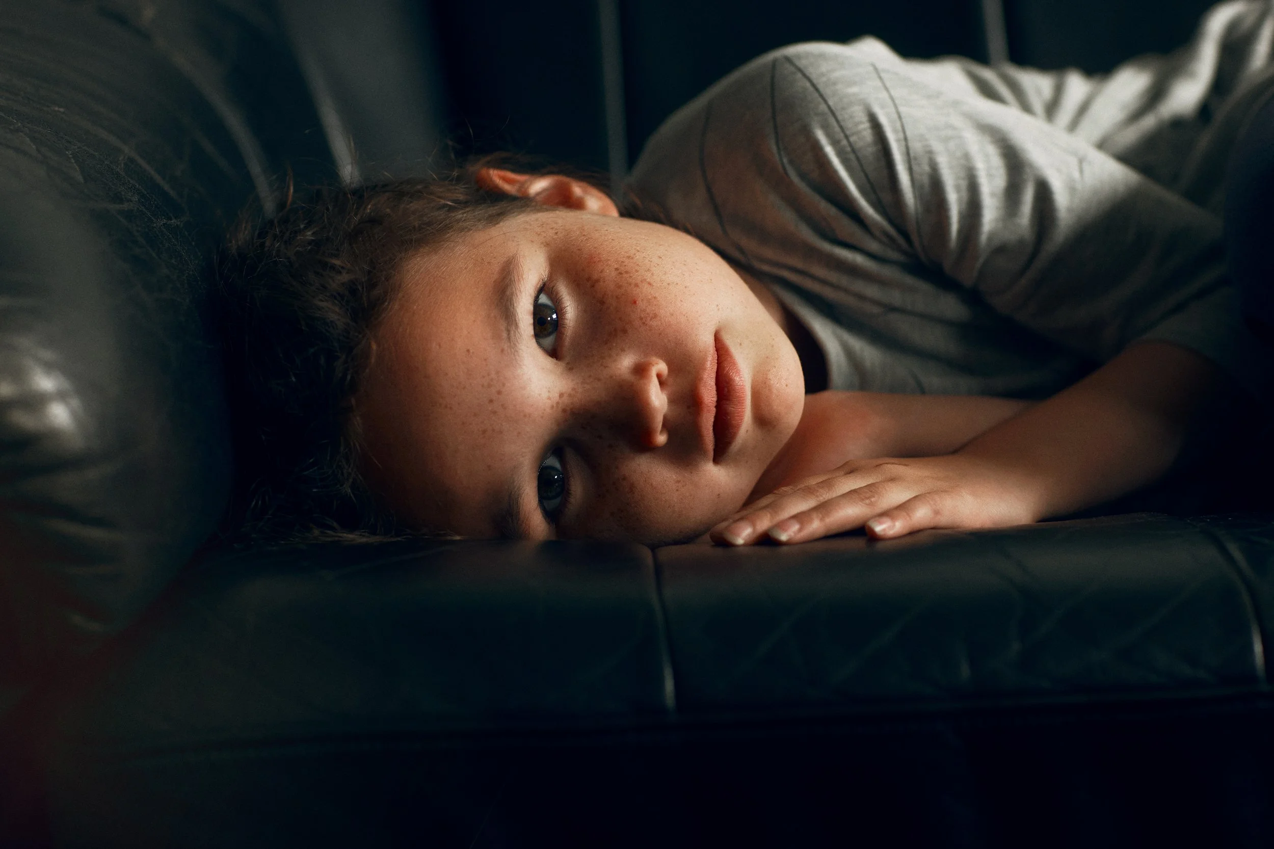 Child lying on sofa looking towards camera, still and reflective moment