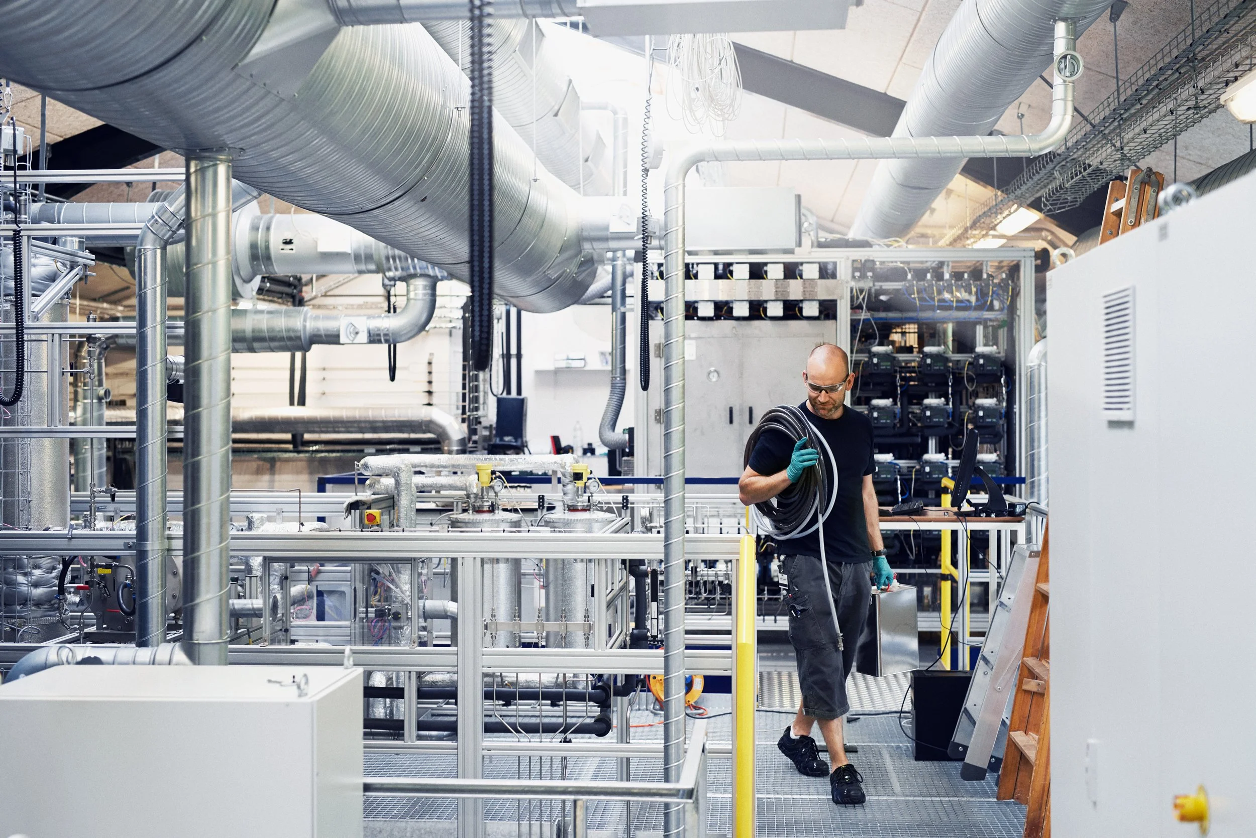 Technician working on industrial equipment in production facility with pipes and machinery