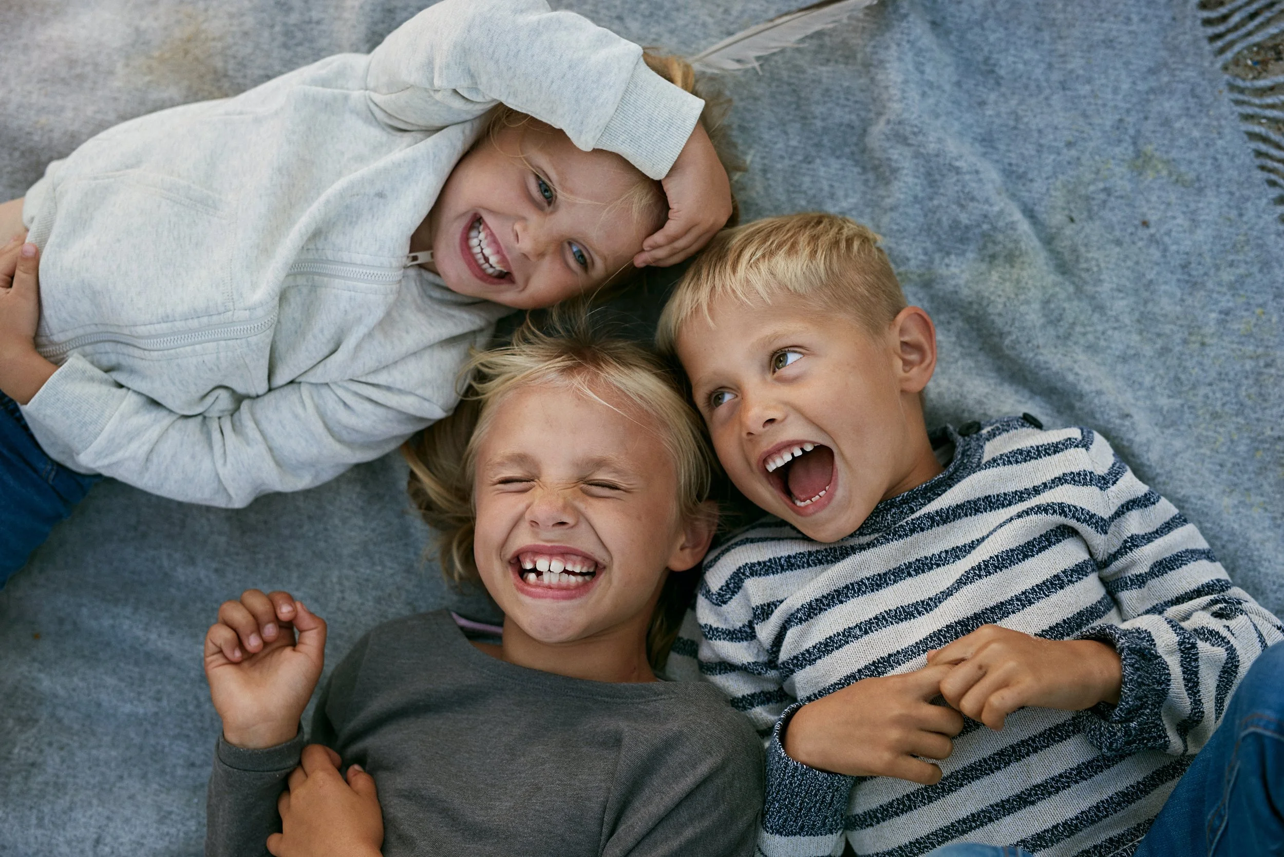 Three children lying together laughing, close social interaction