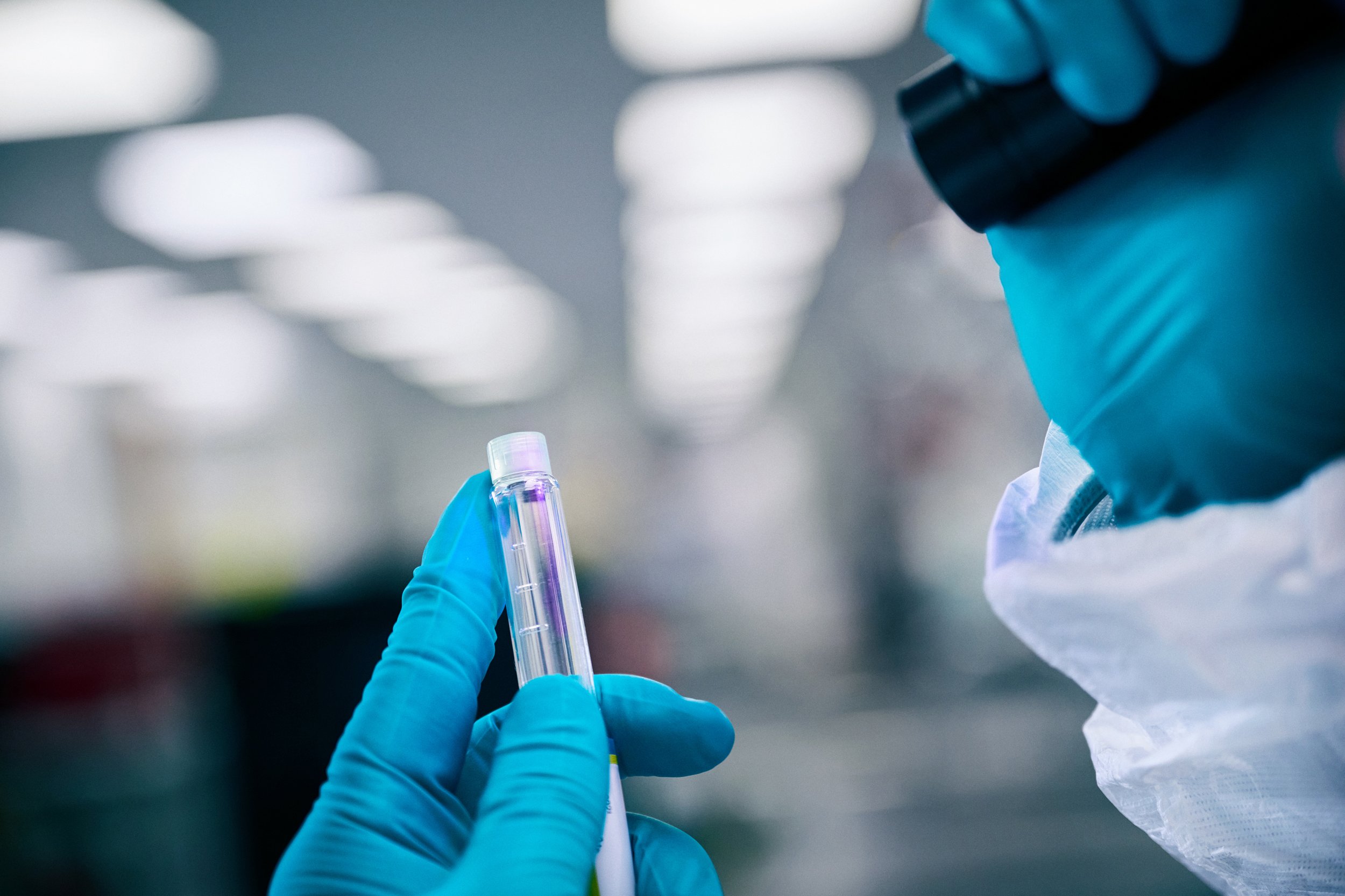Close-up of gloved hands holding test tube under inspection in laboratory
