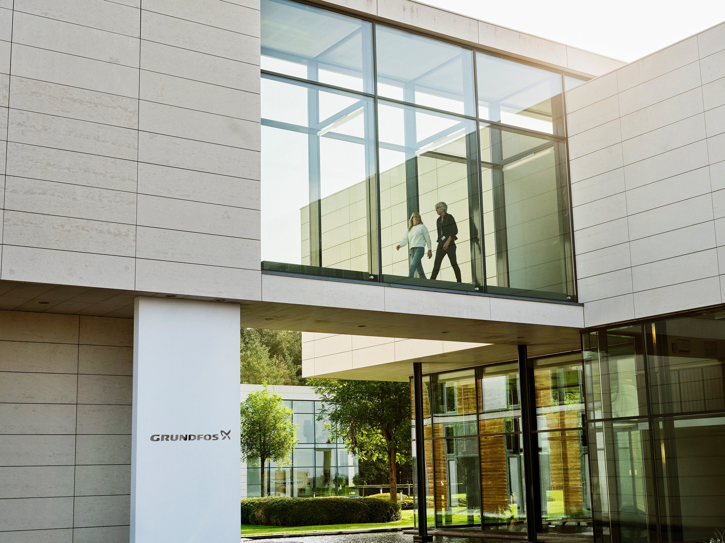 Employees walking across glass bridge inside modern office architecture