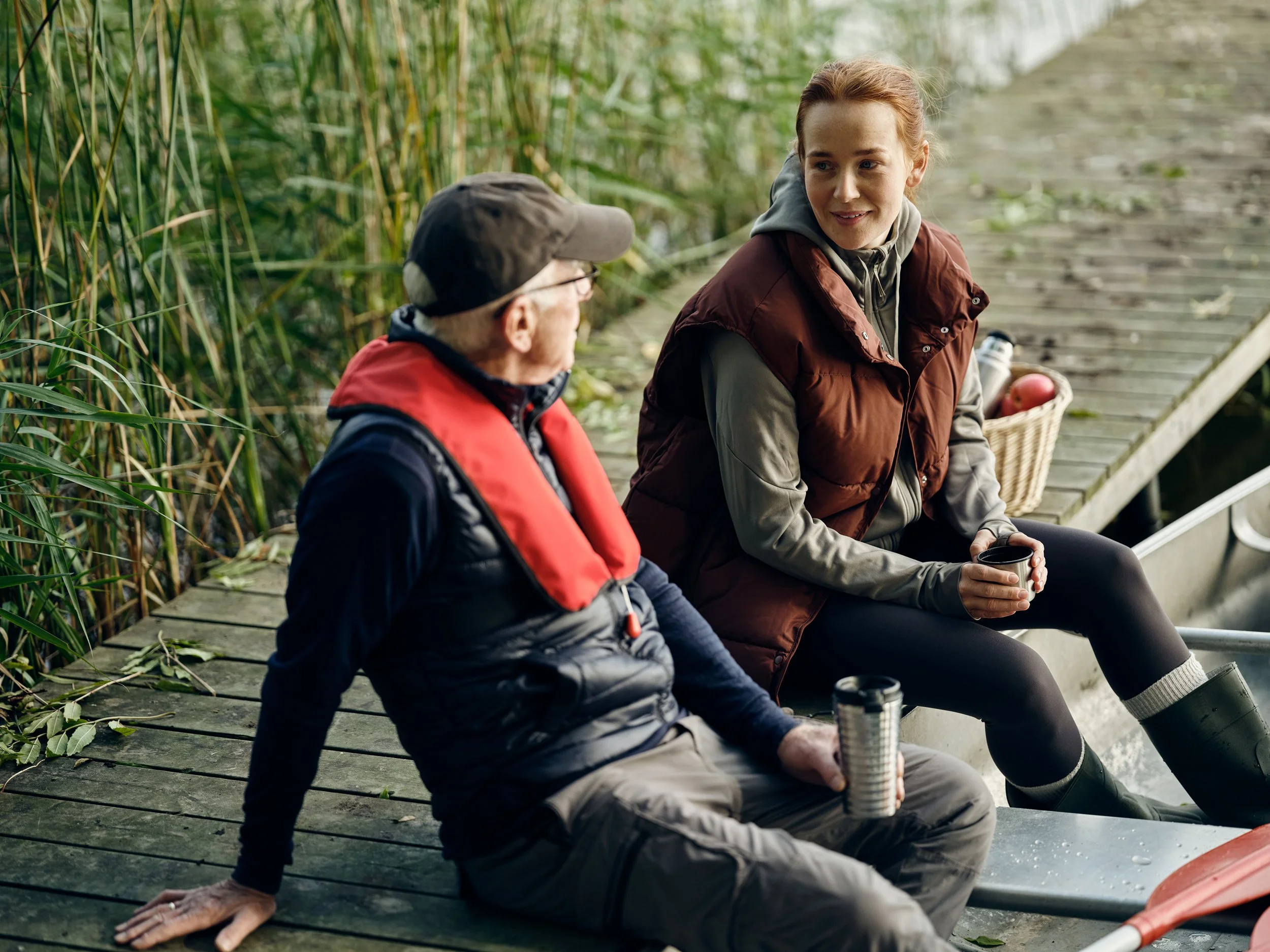 Two people sitting by water with life jackets, pause during outdoor activity