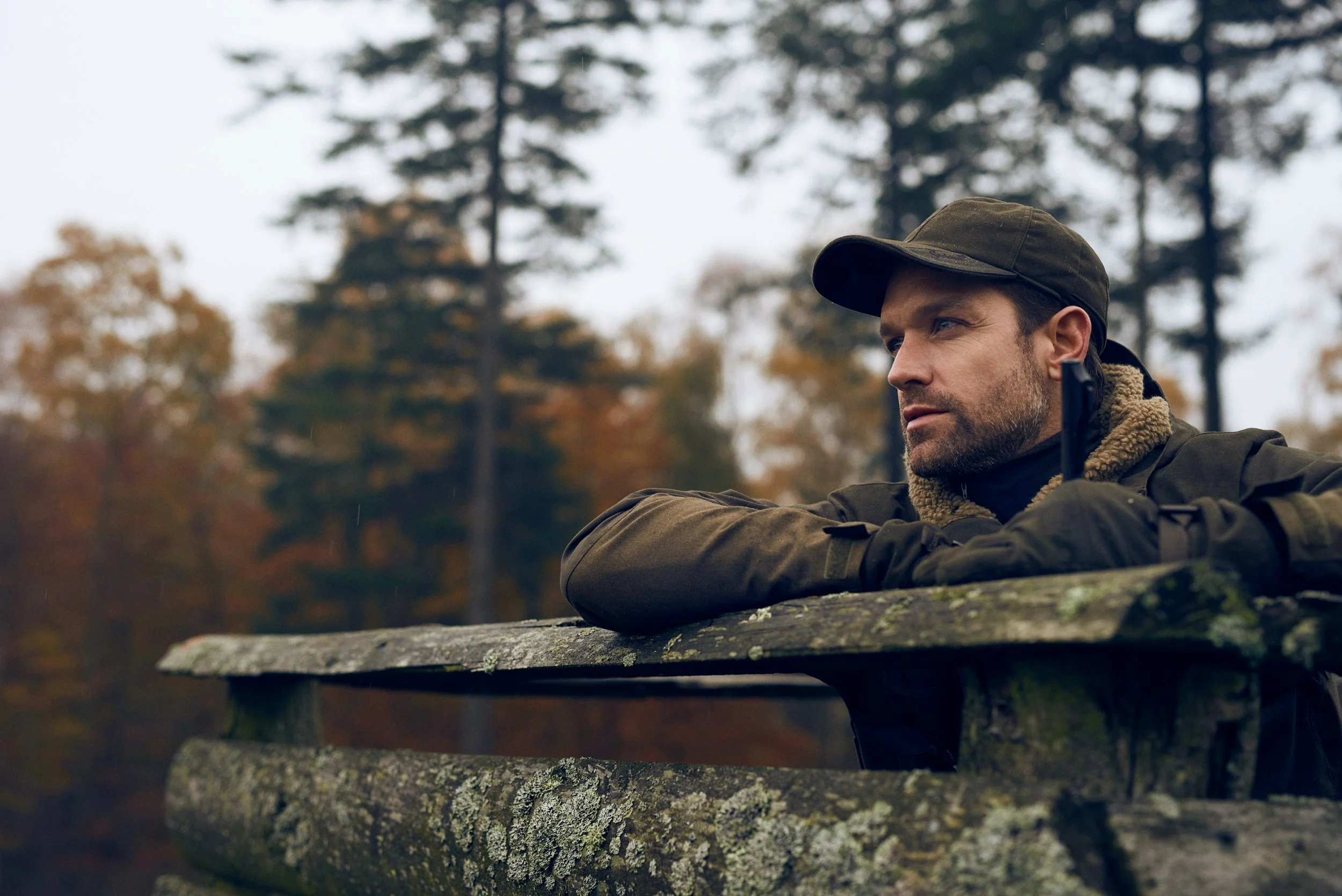 Man leaning on wooden fence in forest, reflective moment in autumn landscape

