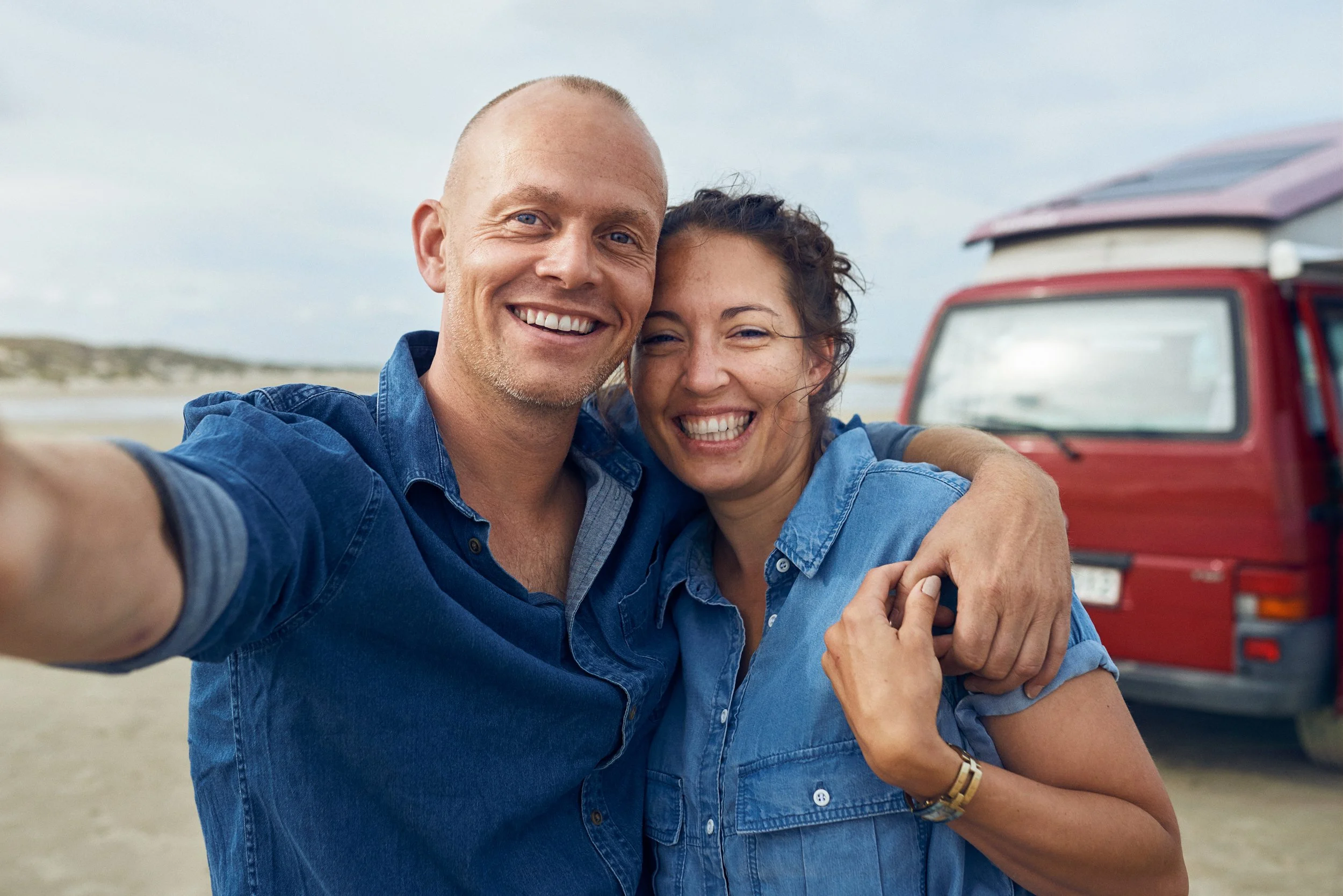Couple taking selfie by van at beach, shared travel moment