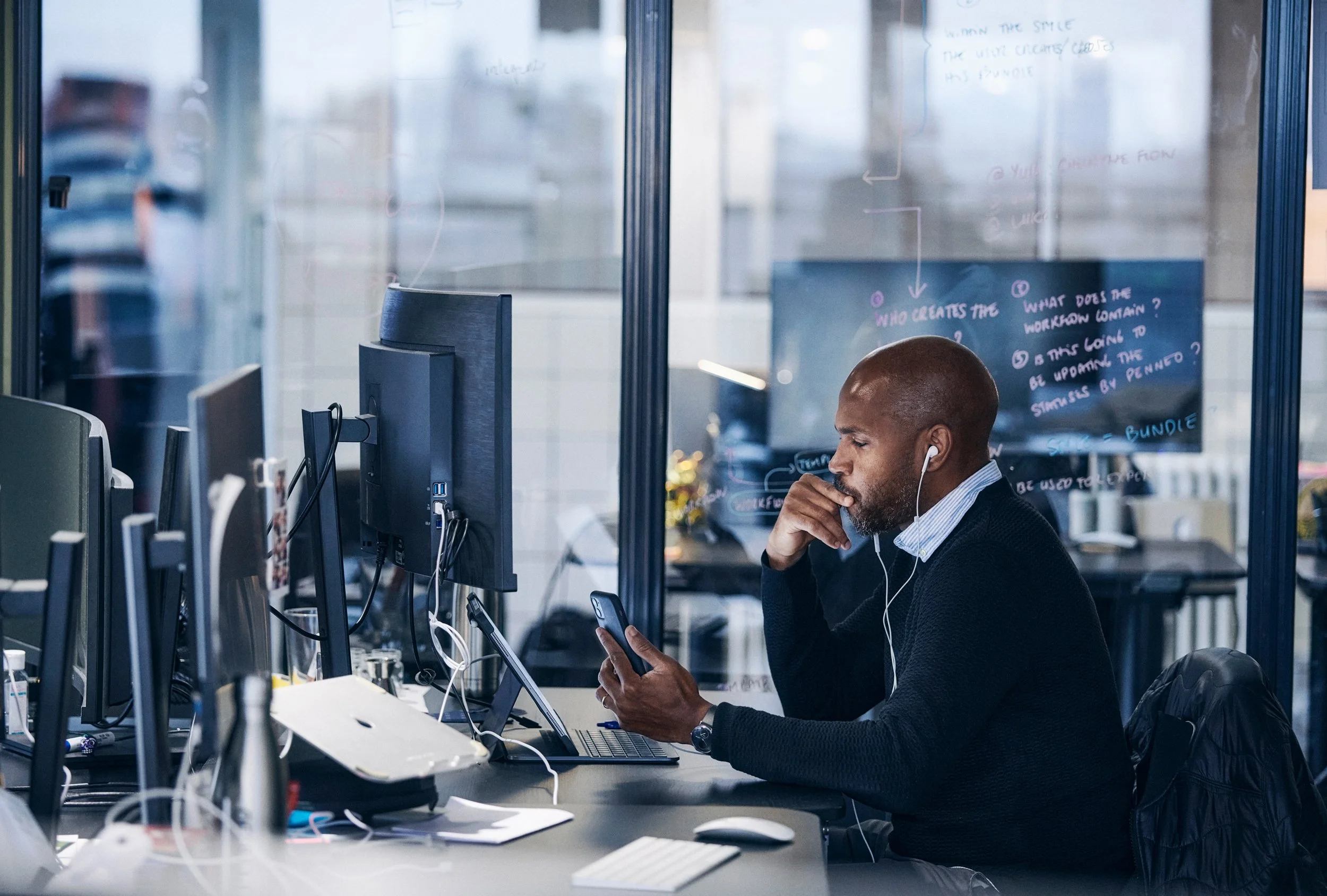 Office worker seated at desk using computer and phone, multitasking in workplace