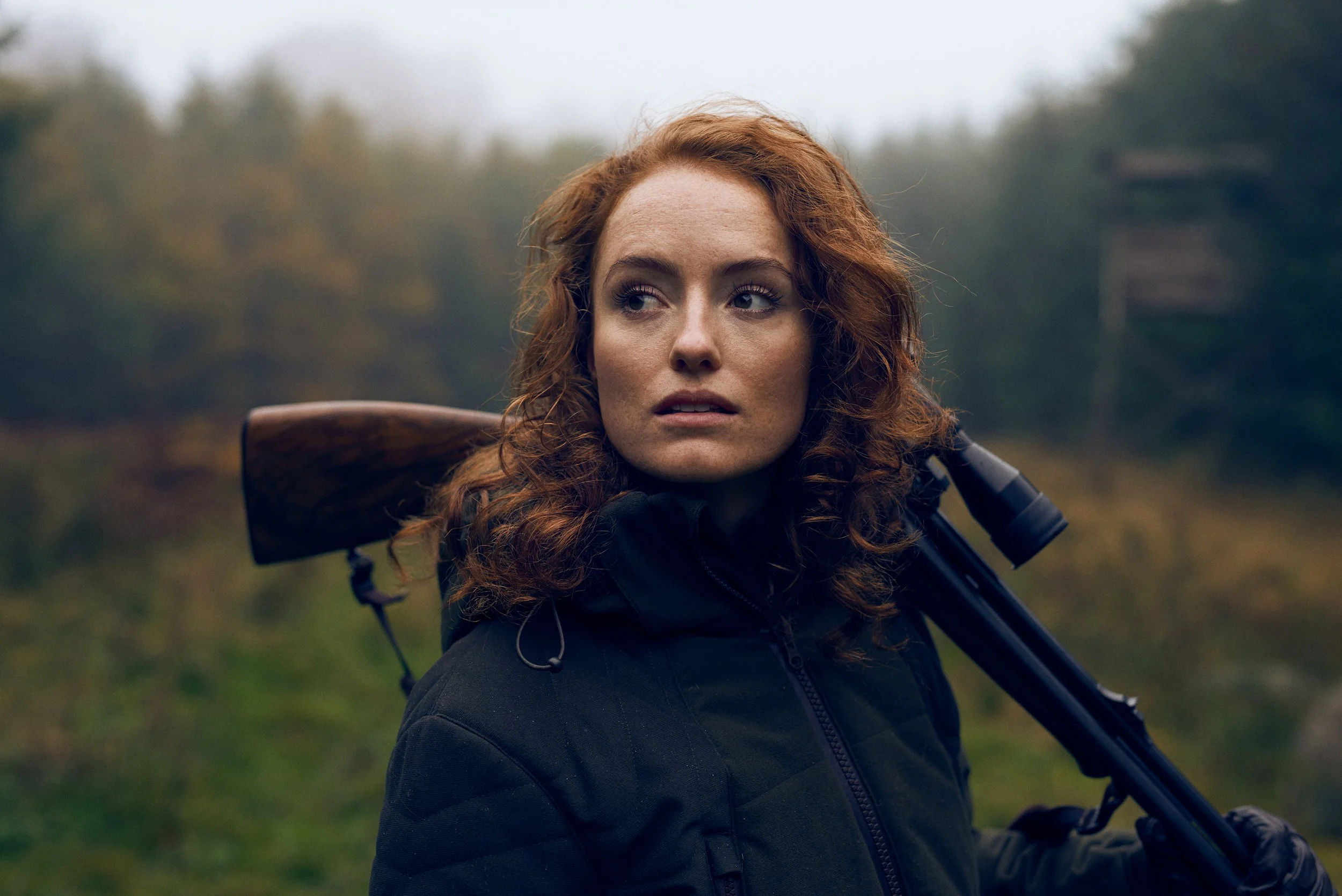 Portrait of woman carrying shotgun over shoulder, forest background and soft light
