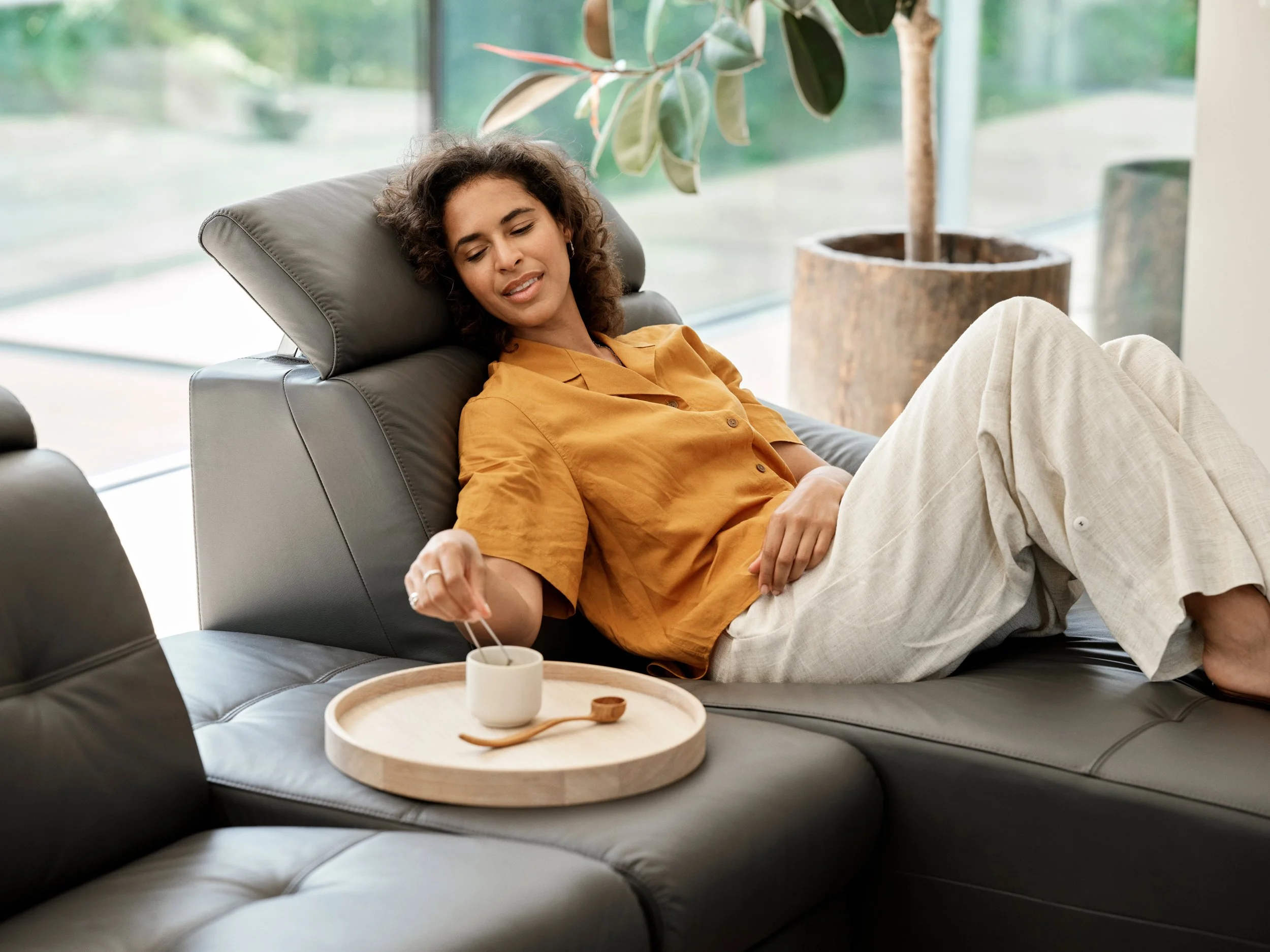 Woman reclining on sofa reaching for cup, calm everyday moment in home