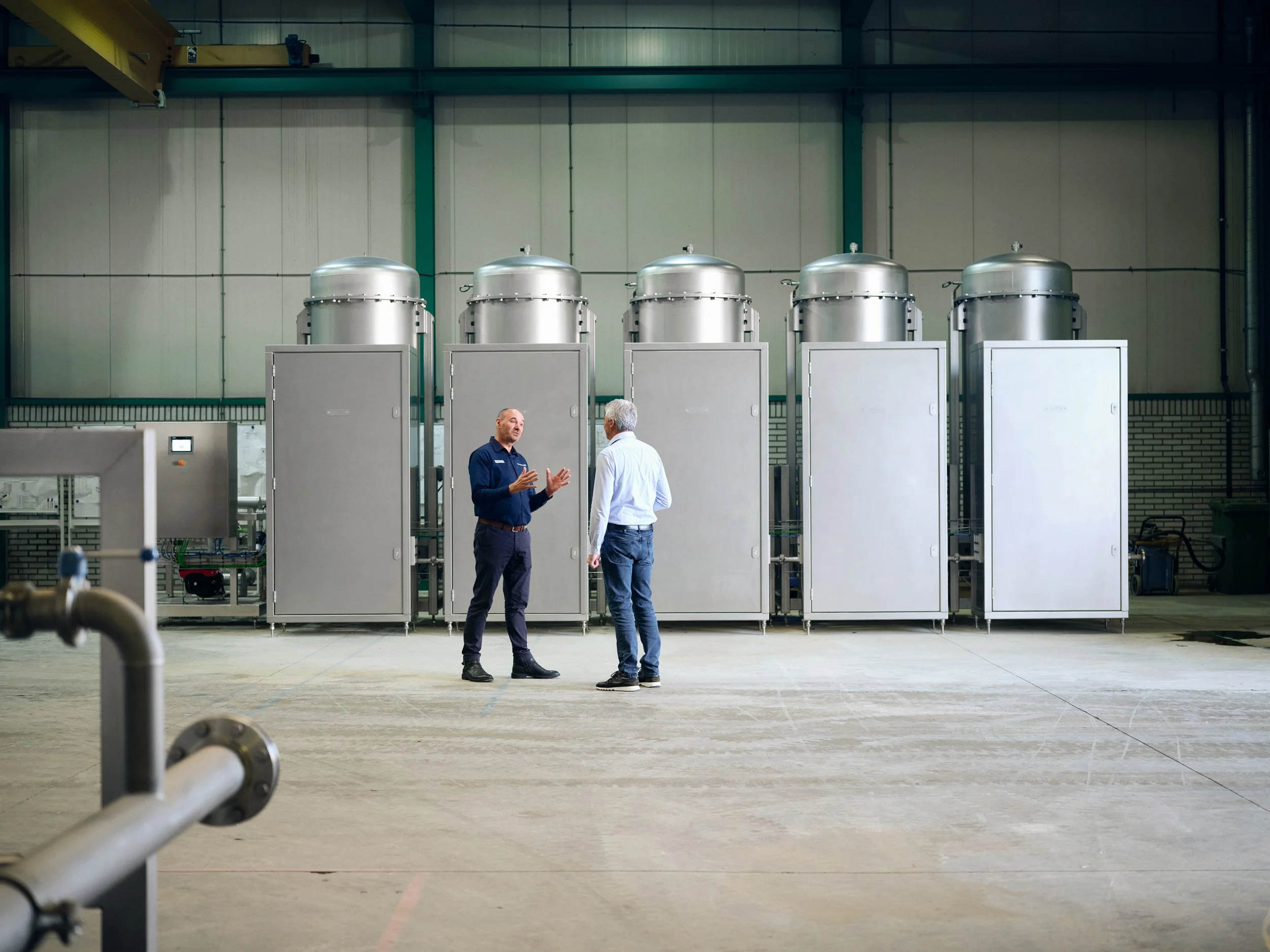 Two men talking in front of large industrial units in production hall