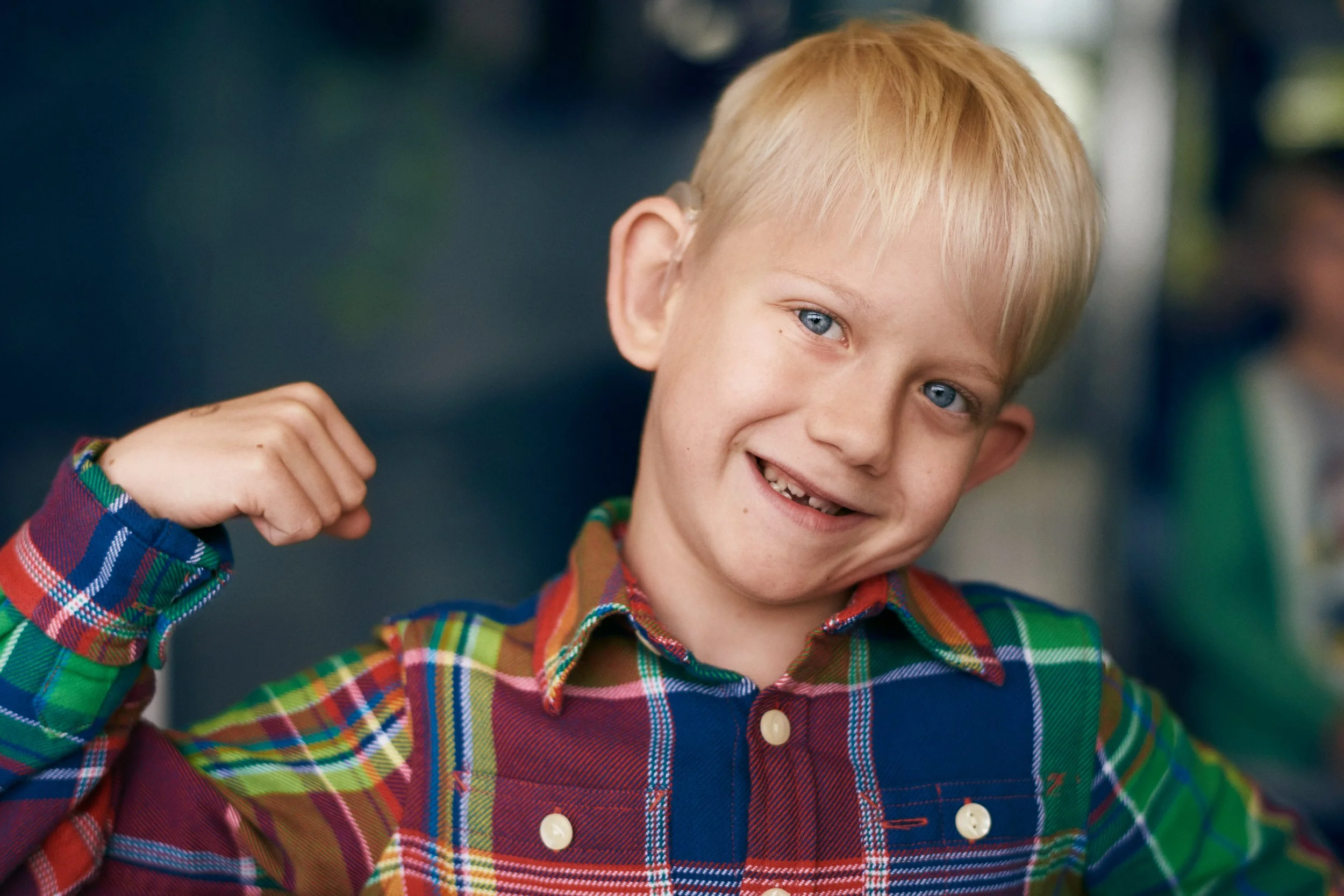Child wearing hearing aid smiling and raising arm, playful expression indoors