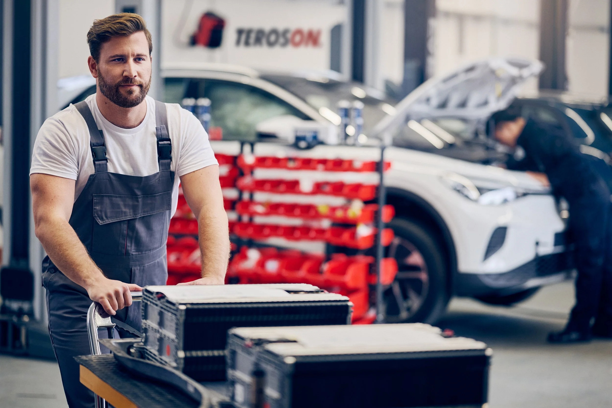 
Technician working in automotive workshop with tools and vehicle in background