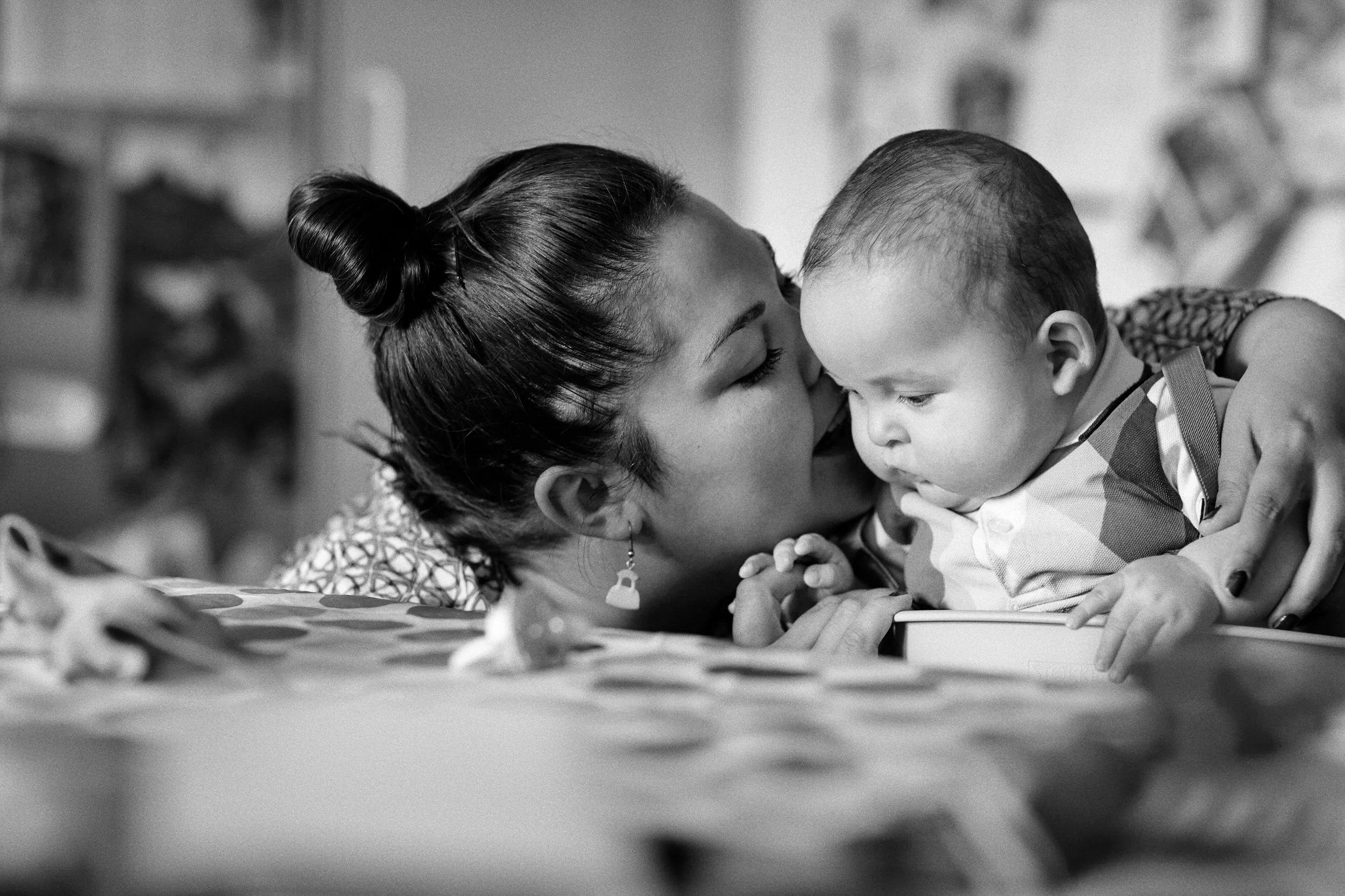 Woman holding baby close and kissing forehead, intimate moment indoors
