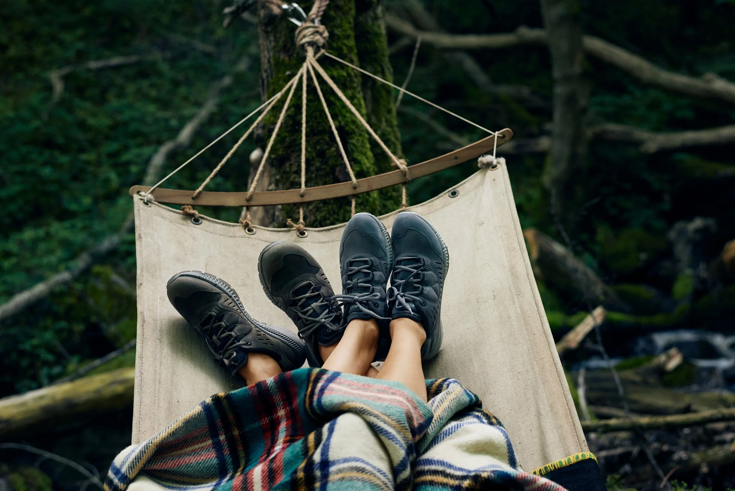 Feet resting in hammock wearing outdoor shoes, forest setting