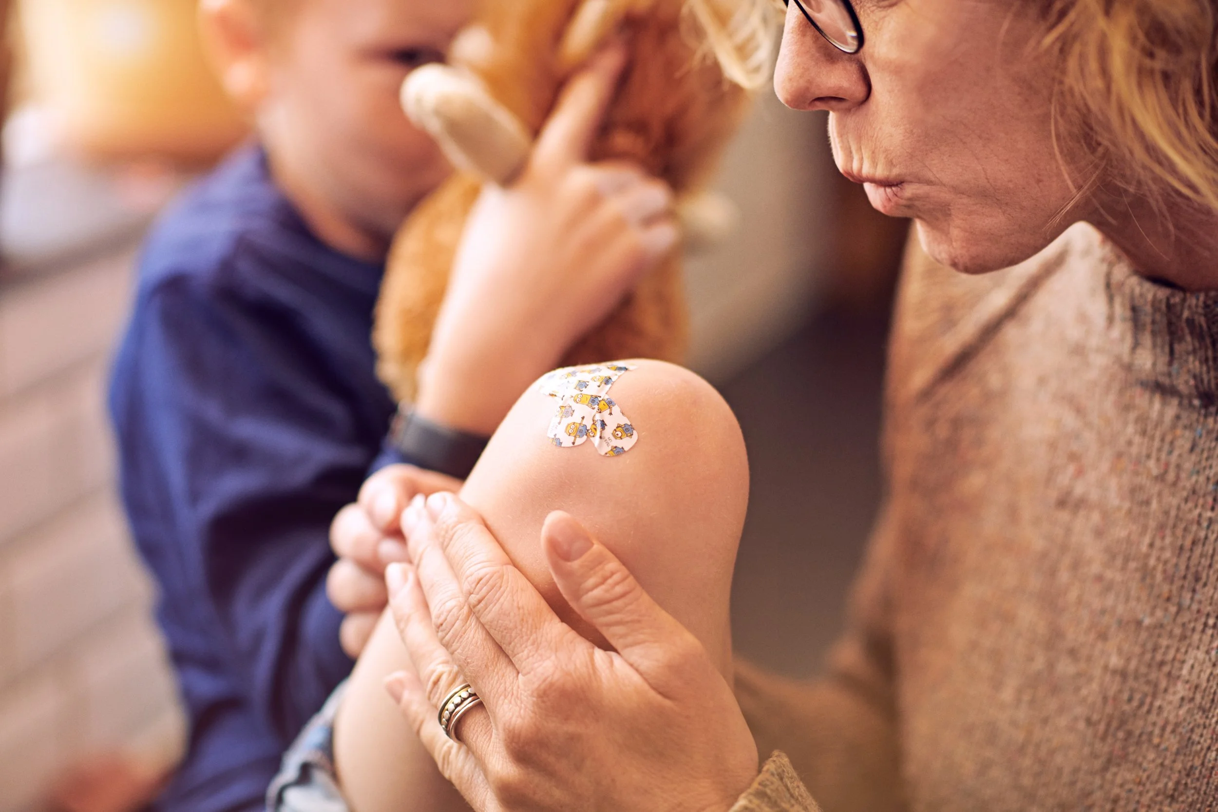 Adult applying bandage to child’s knee, minor injury care at home