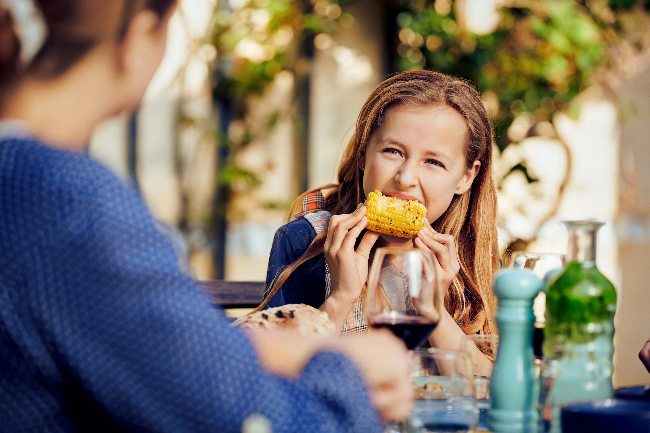 Girl eating corn at outdoor table, everyday food moment