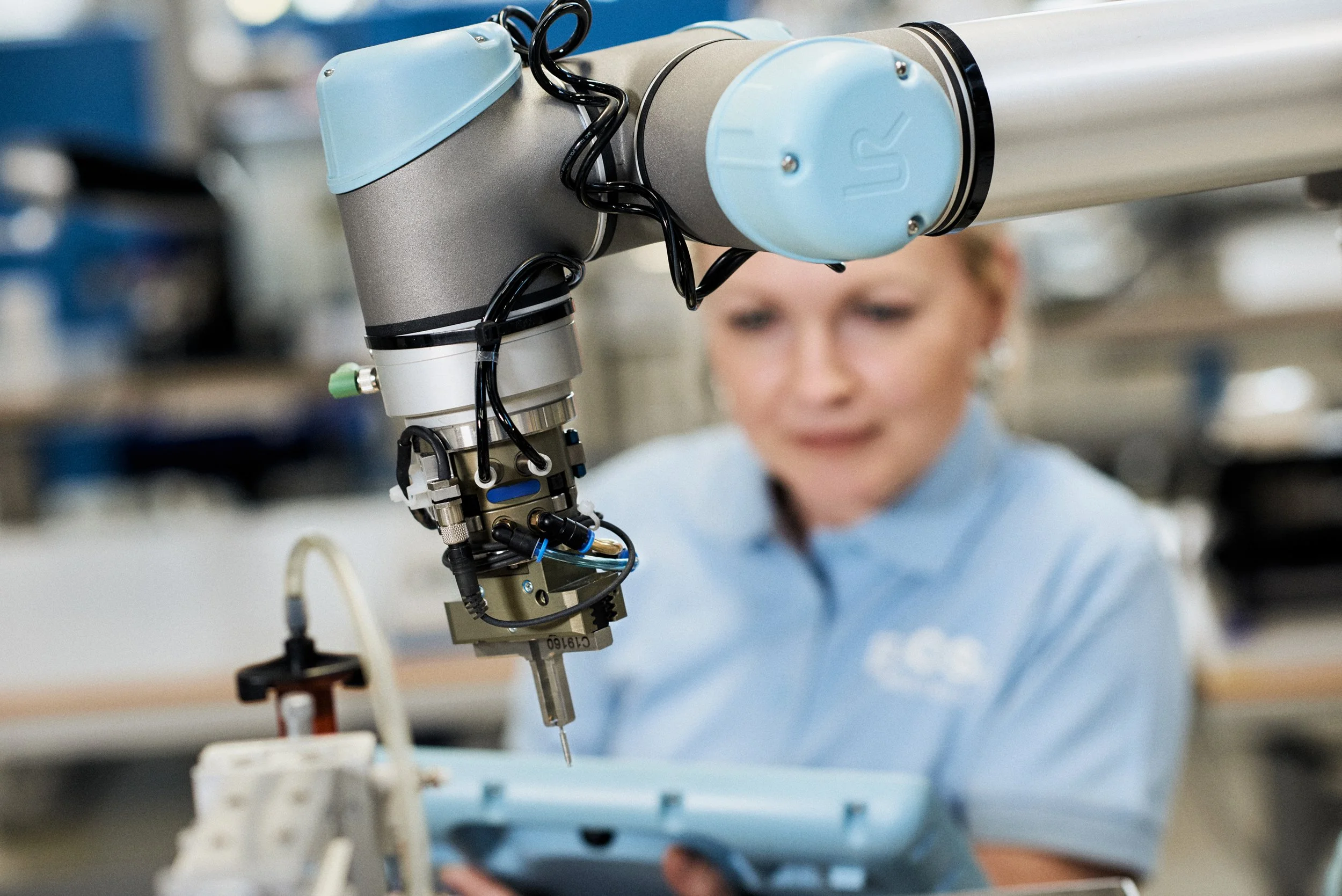 Close-up of collaborative robot arm performing precision task with operator monitoring in background 