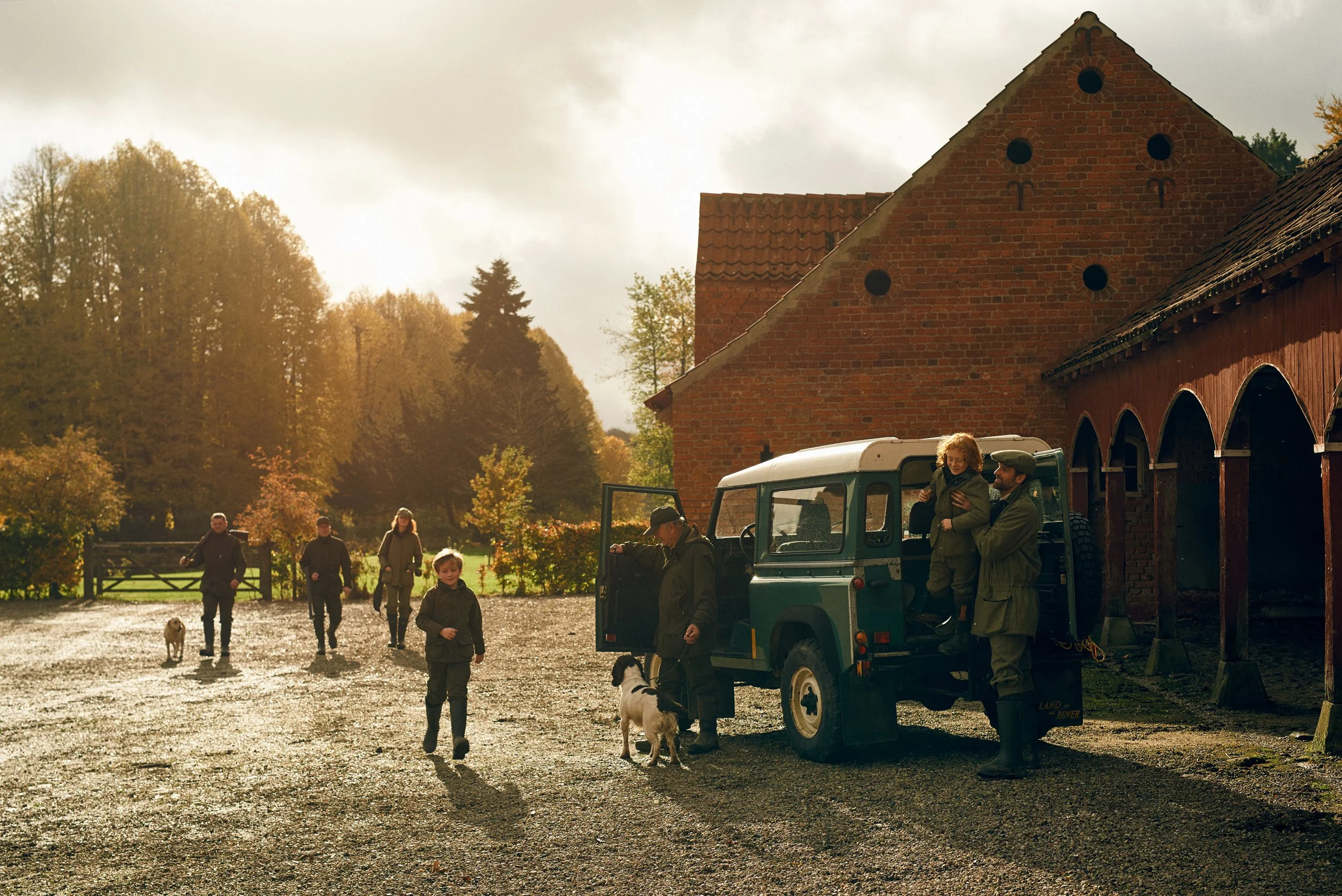 Group gathered near farm buildings with dogs and vehicle, social moment around hunting day