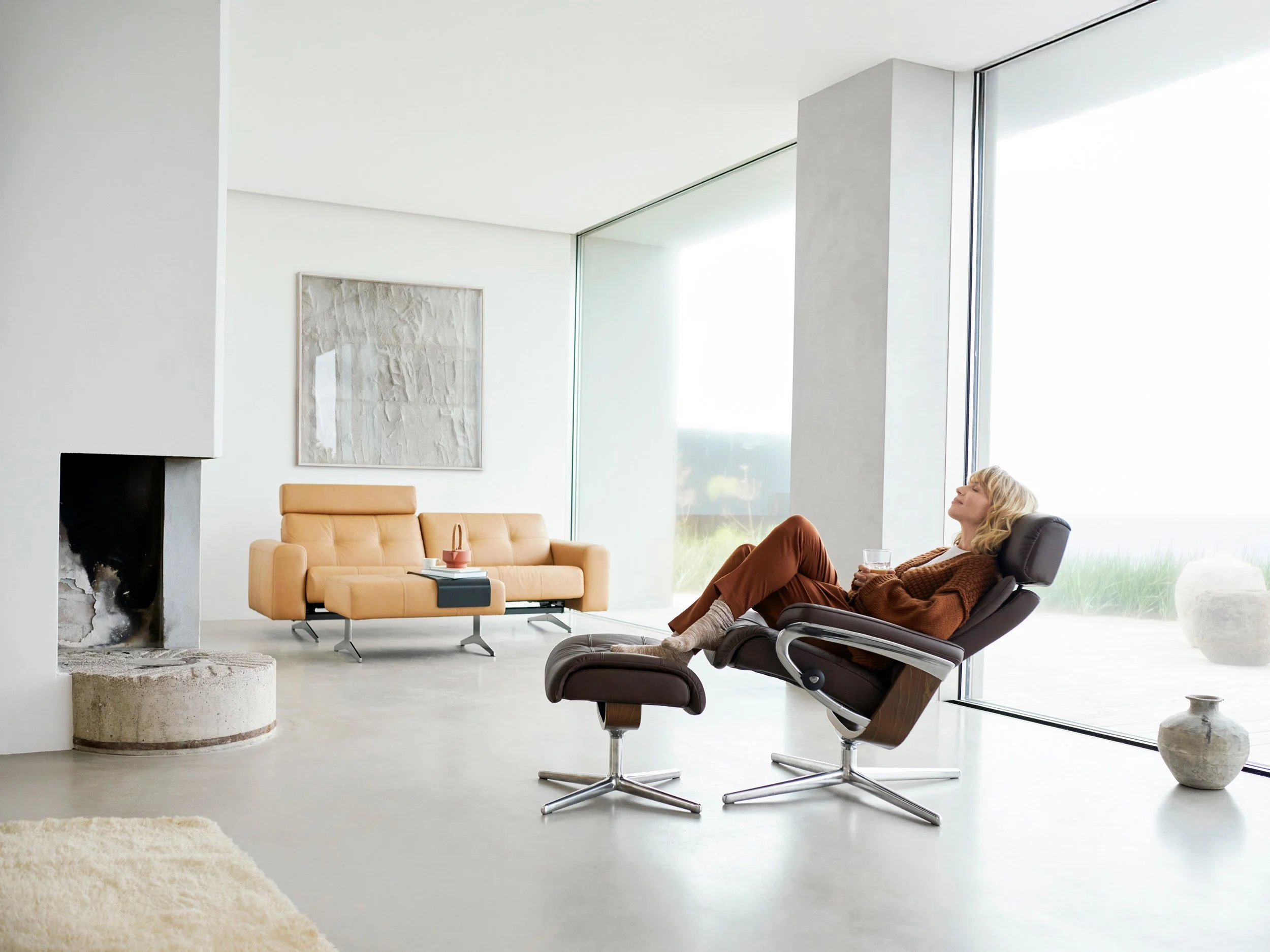 Woman reclining in chair with footstool in minimal living room, resting in daylight