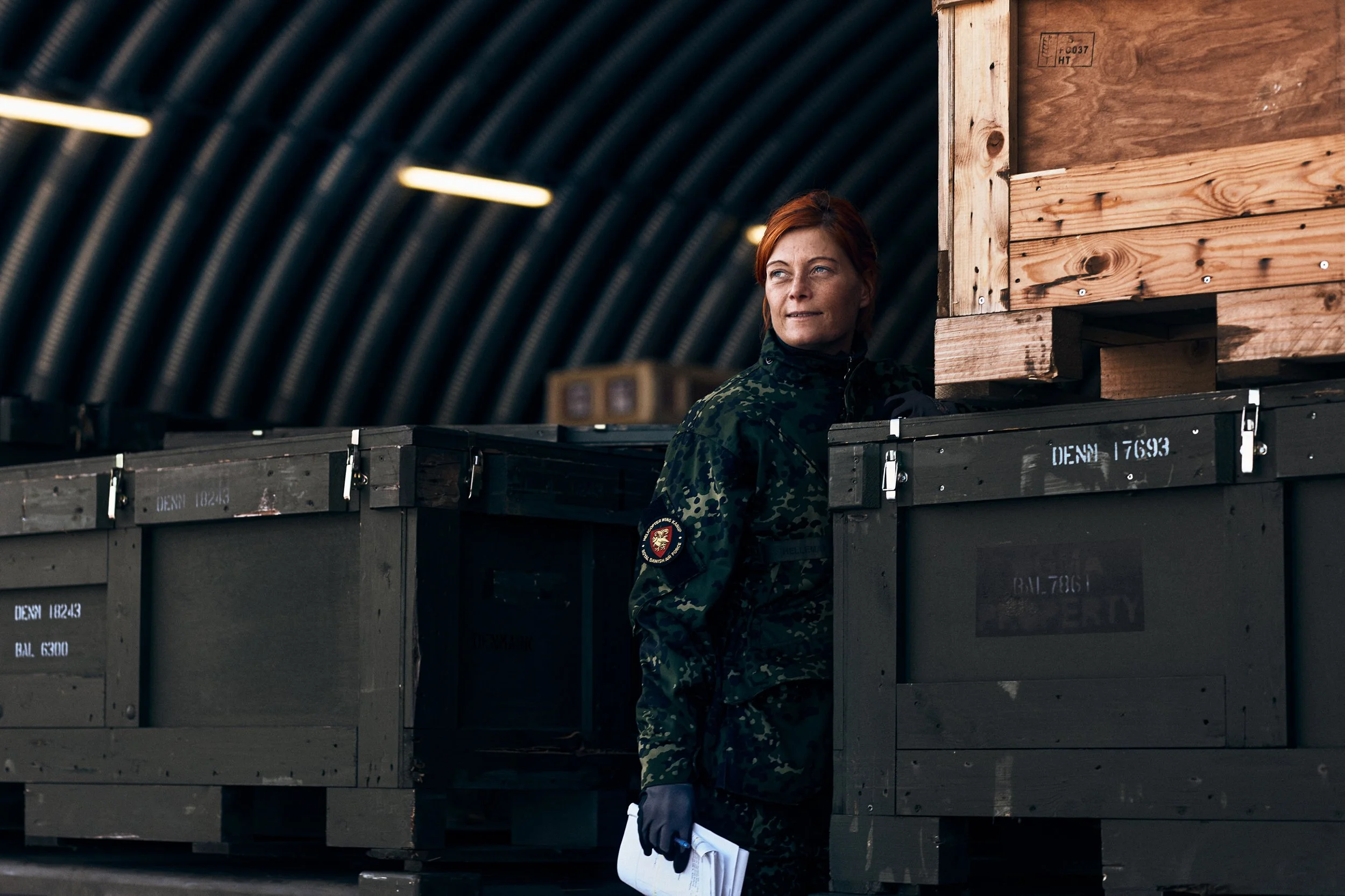 Soldier standing between military storage crates inside hangar holding documents