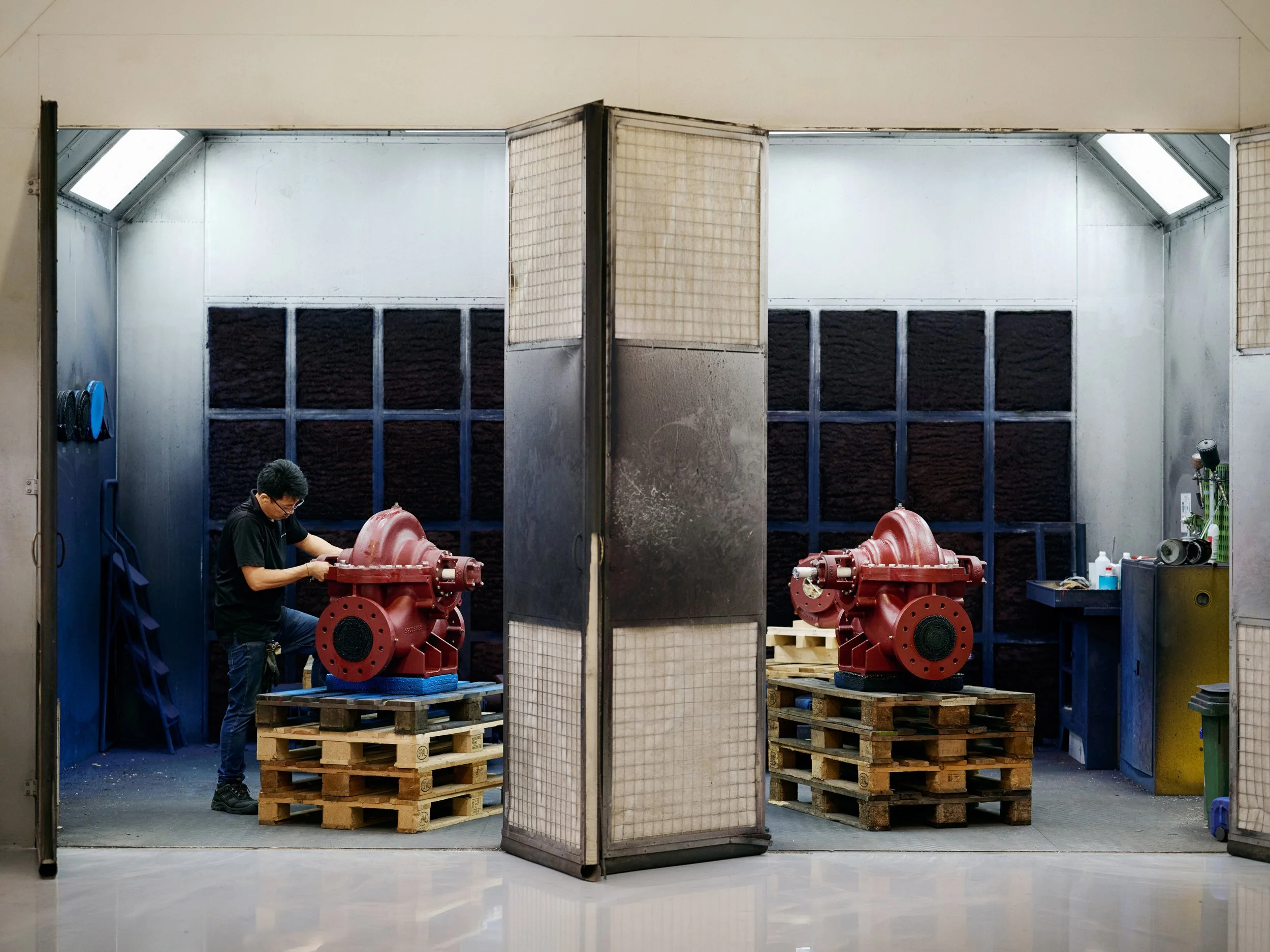 Two large pump units placed on pallets inside testing or treatment chambers, technician working on one