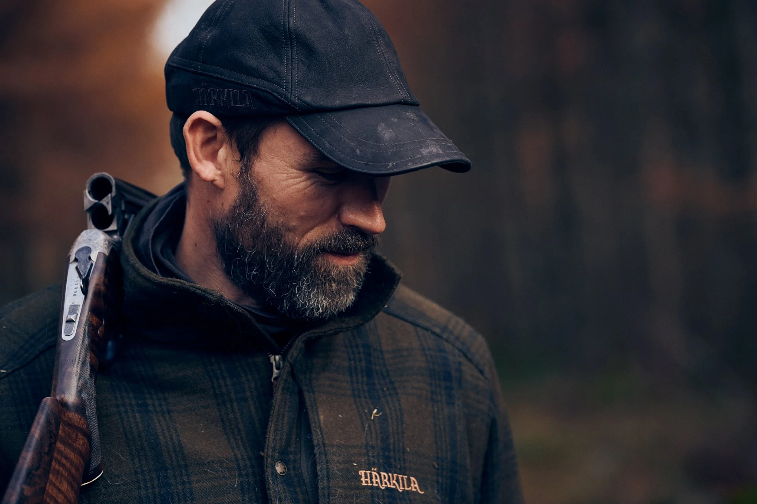 Hunter looking down while carrying rifle over shoulder, calm moment outdoors