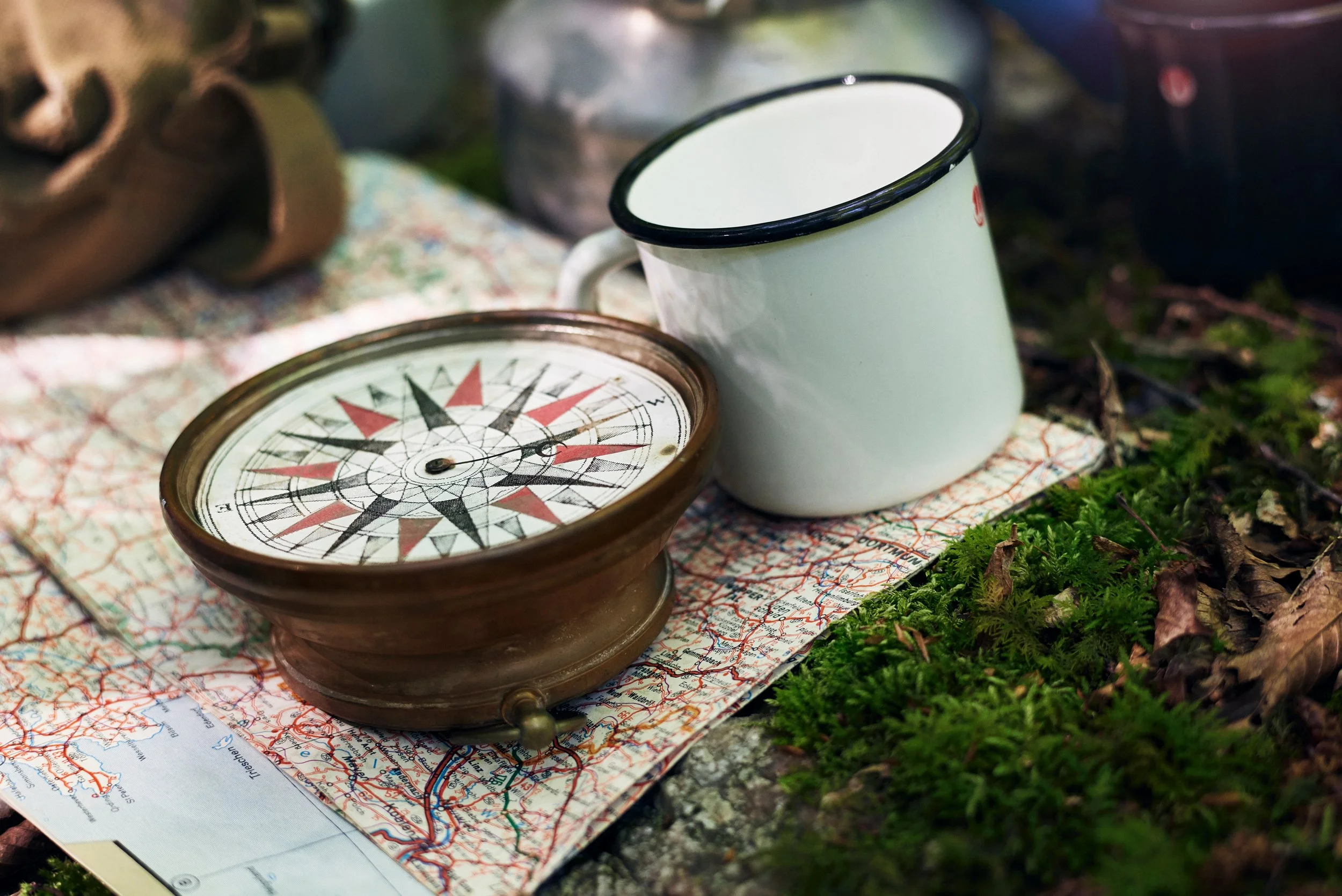 Compass and enamel mug on map in forest, navigation and outdoor gear