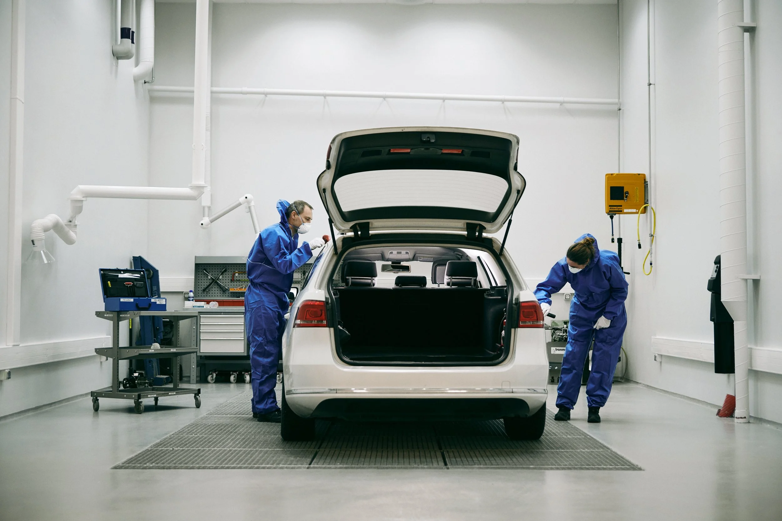 Two forensic technicians inspecting vehicle in workshop with open trunk