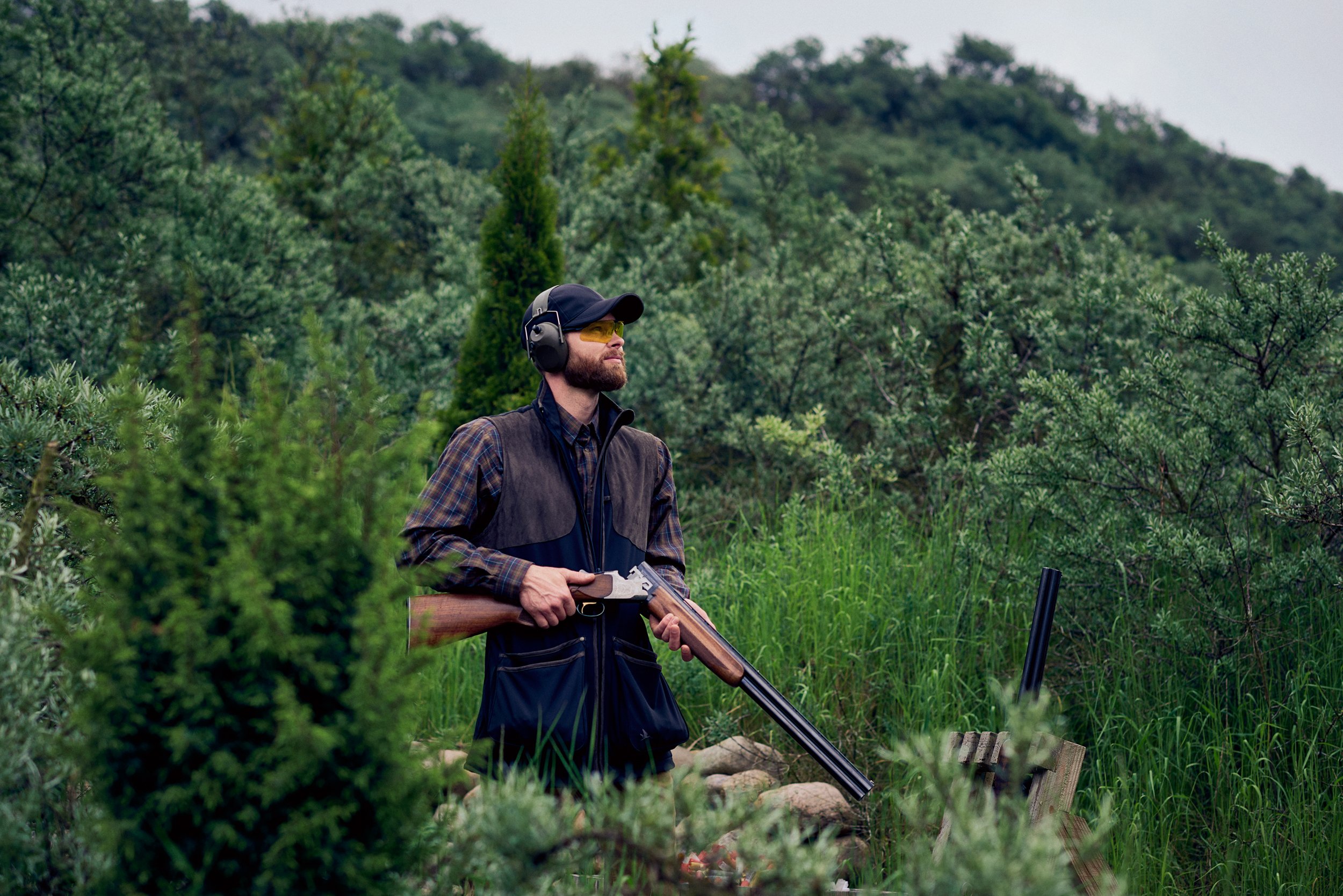 Hunter standing in tall grass holding shotgun, focused moment in outdoor terrain