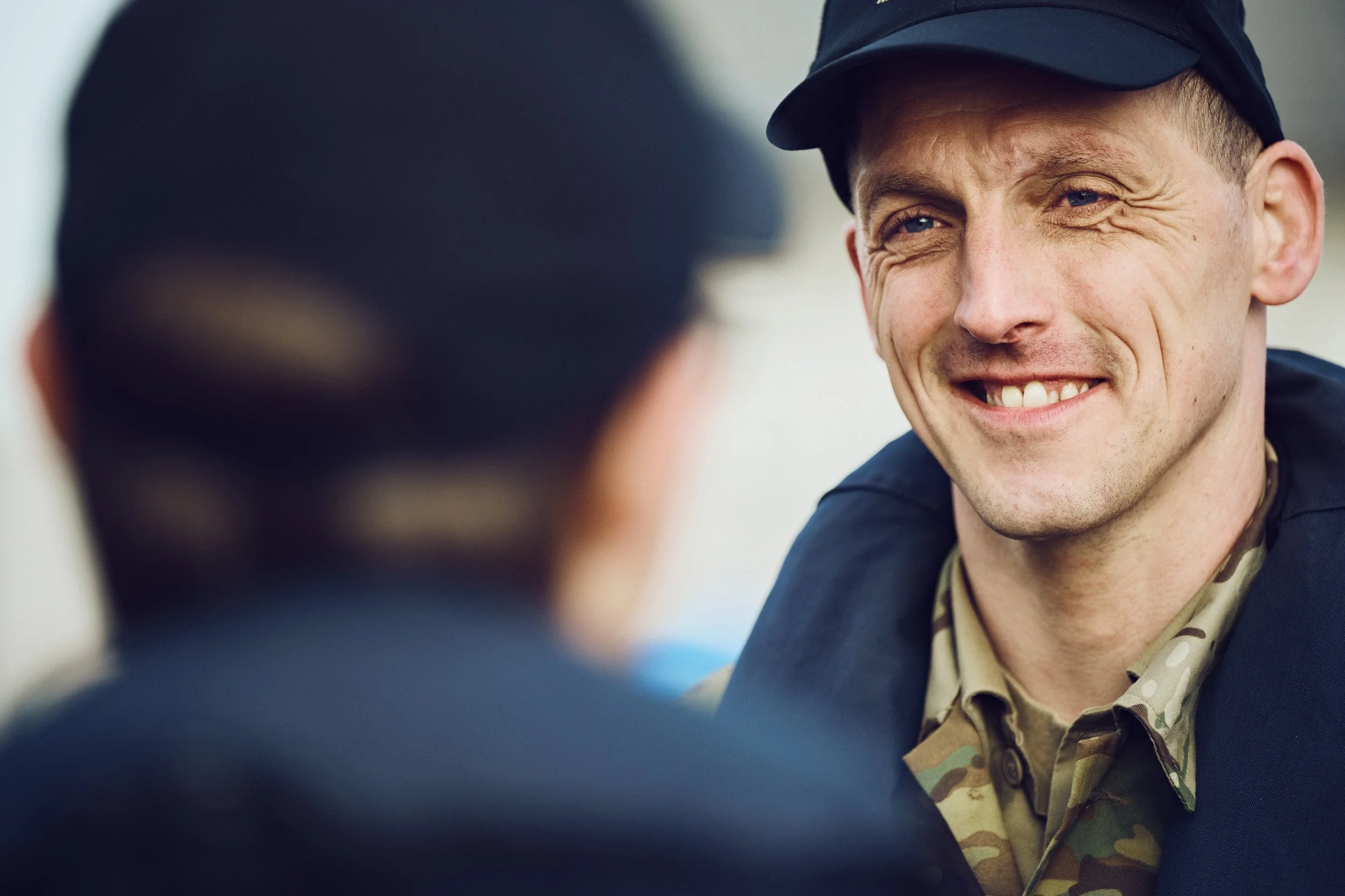 Close-up portrait of Danish Home Guard soldier smiling, shallow depth of field with colleague out of focus in foreground
