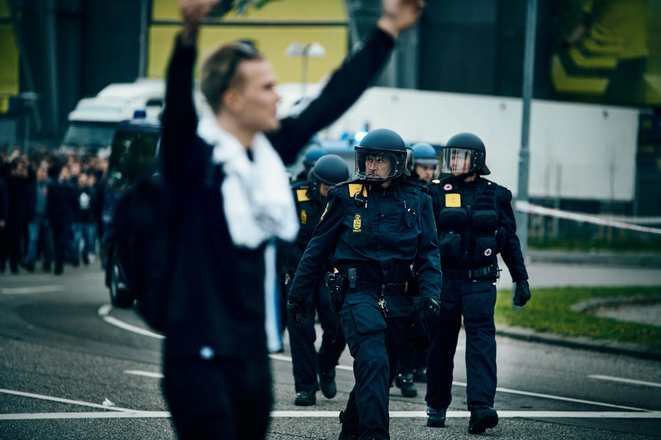 Out of focus person in foreground with riot police officers walking in street outside football stadium