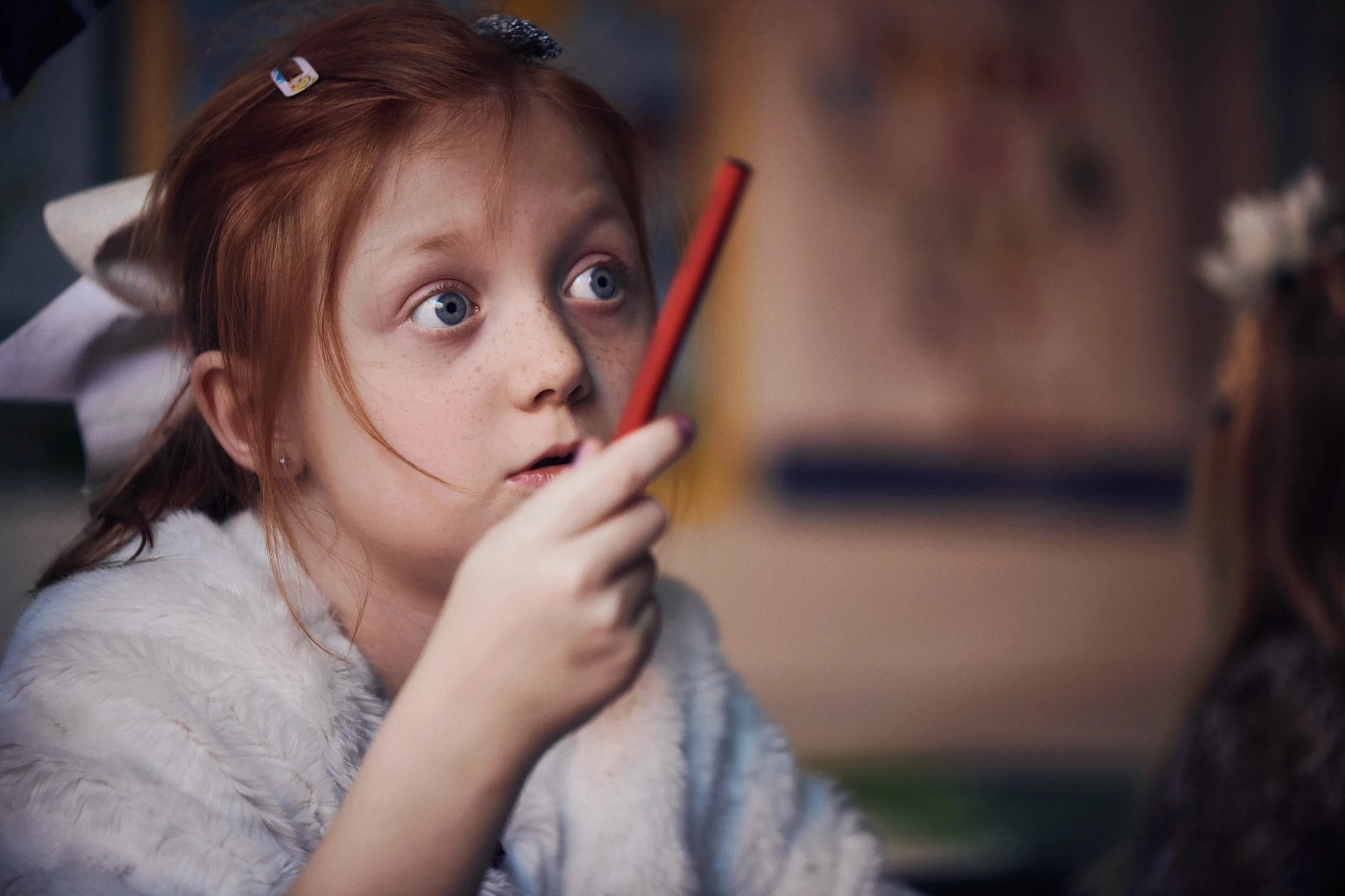 Child holding pencil indoors, focused expression during school activity