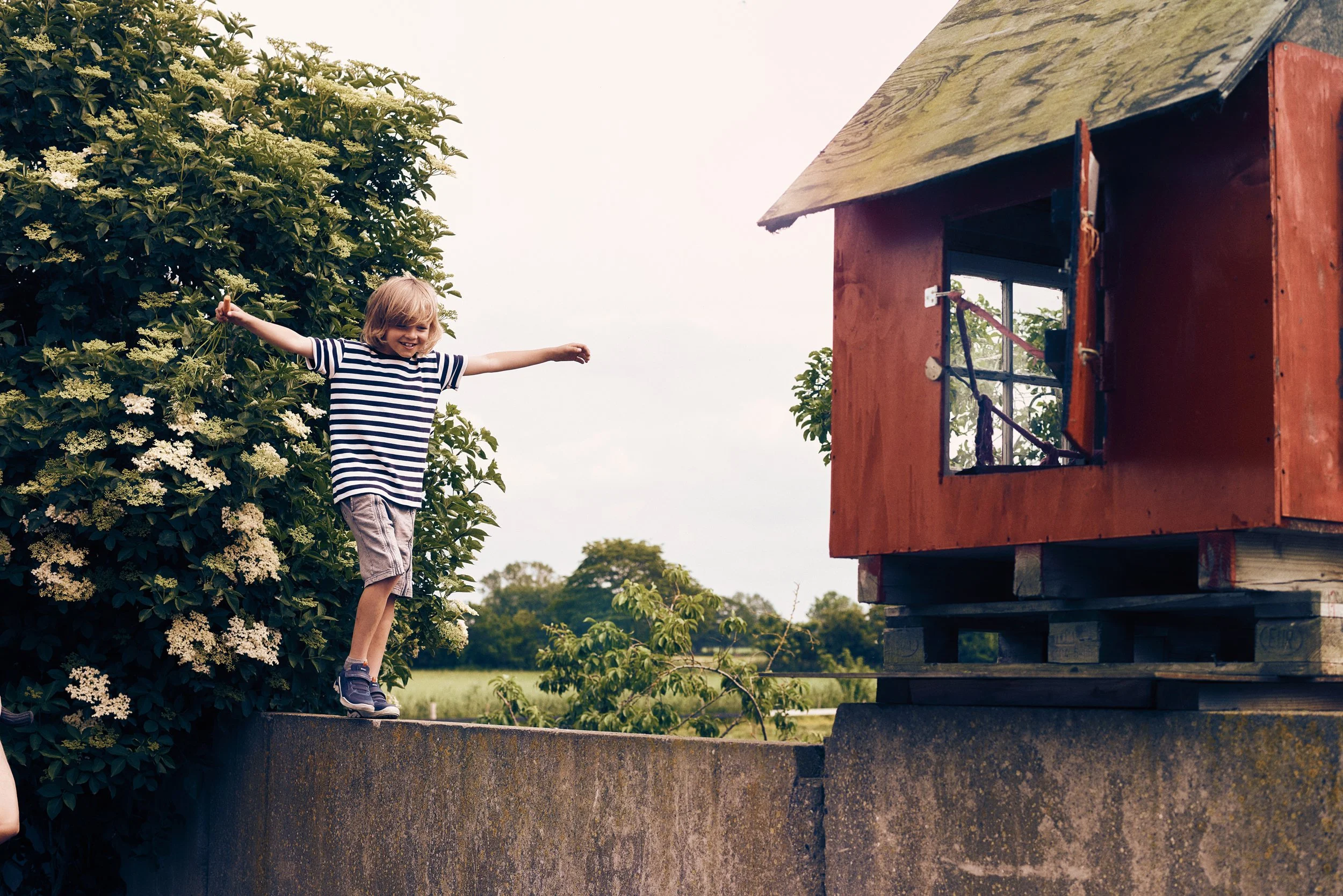 Child balancing on wall near small wooden house, outdoor play