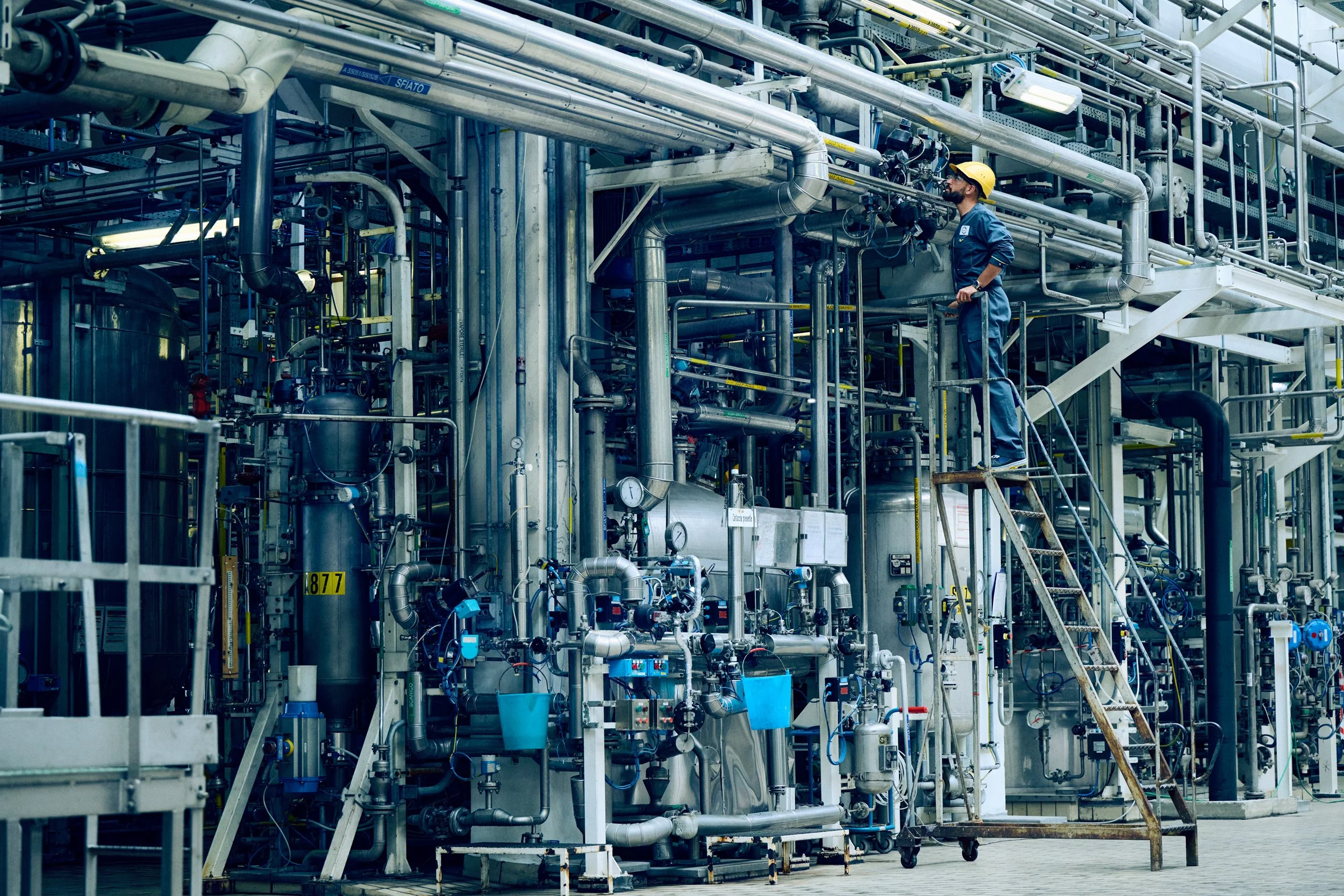 Technician working within complex pipe system, part of industrial production setup