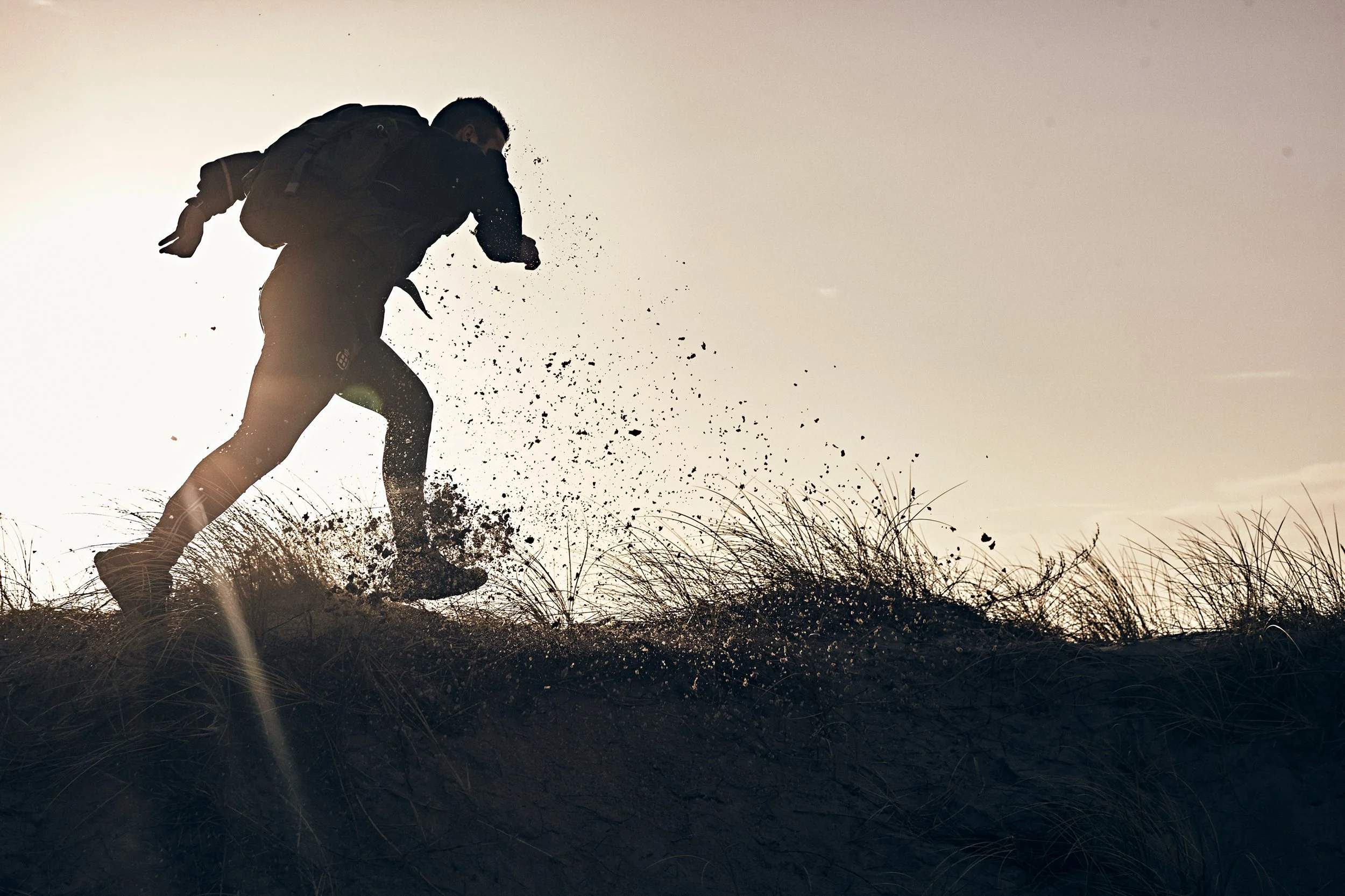 Silhouette of person running over sand dune with backpack