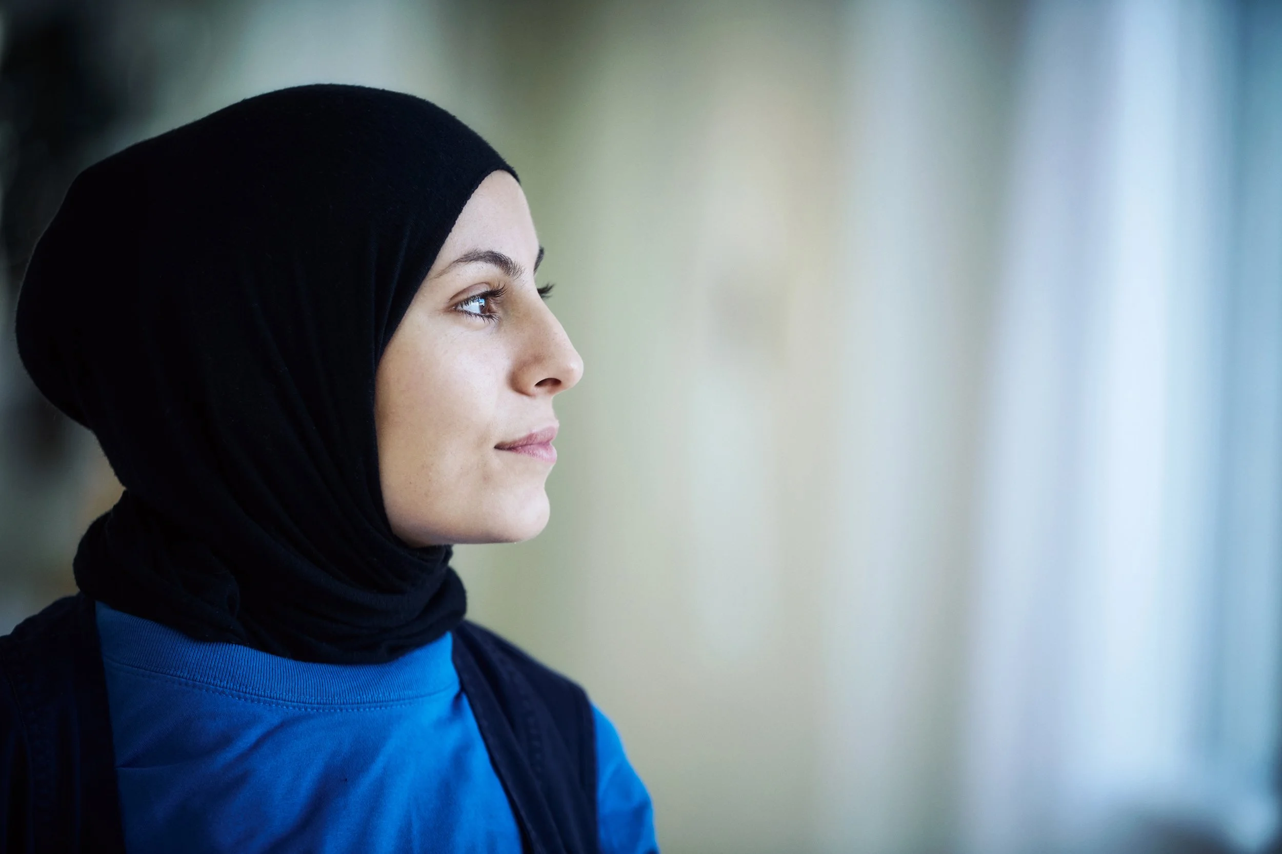 Woman wearing headscarf looking out of window, quiet reflective moment