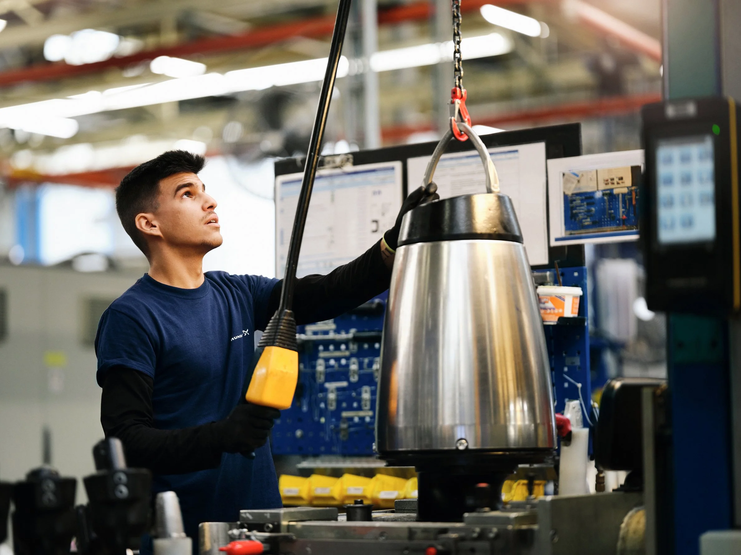 Factory worker operating lifting equipment to position metal pump component during testing
