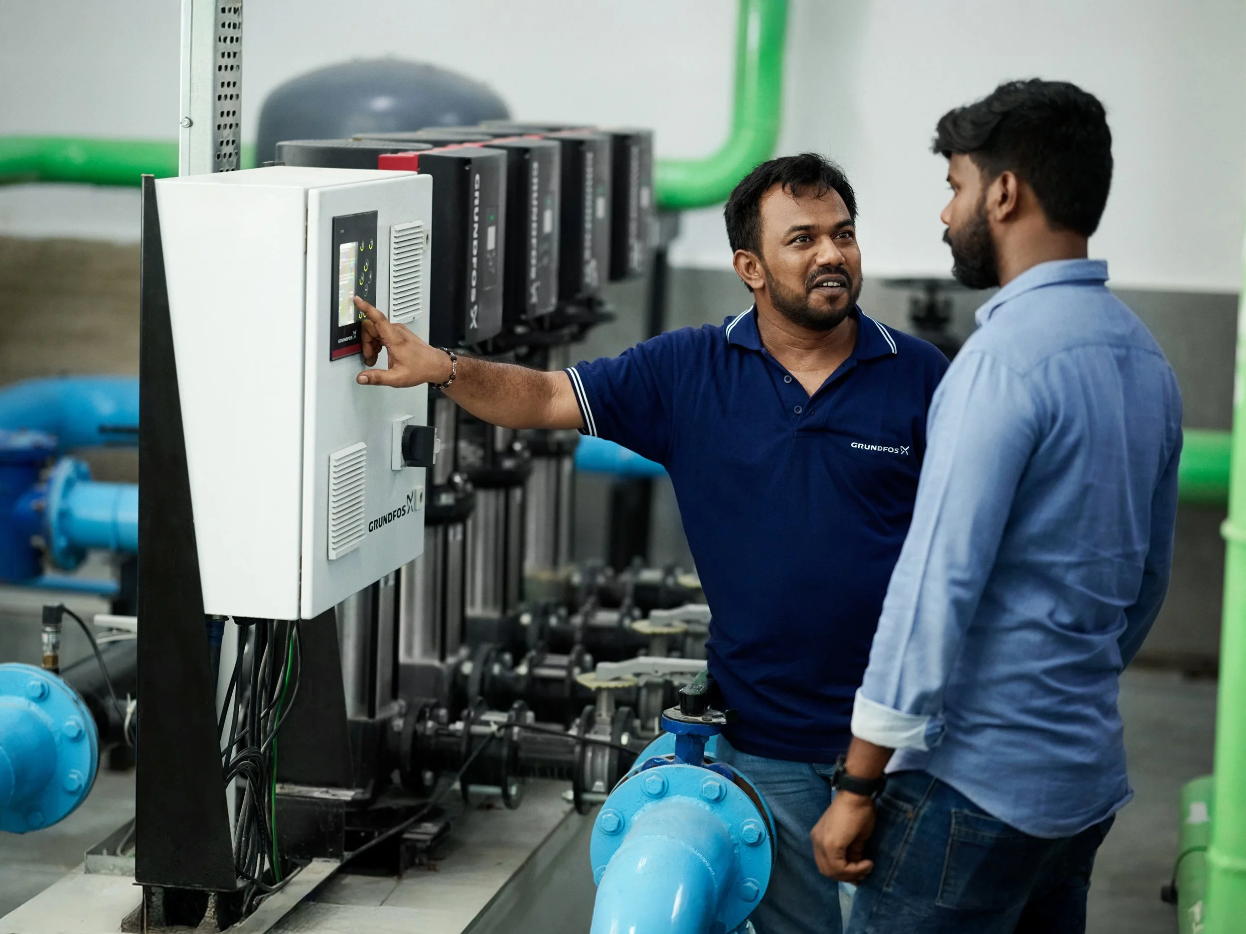 Technician explaining control panel to colleague in pump installation room