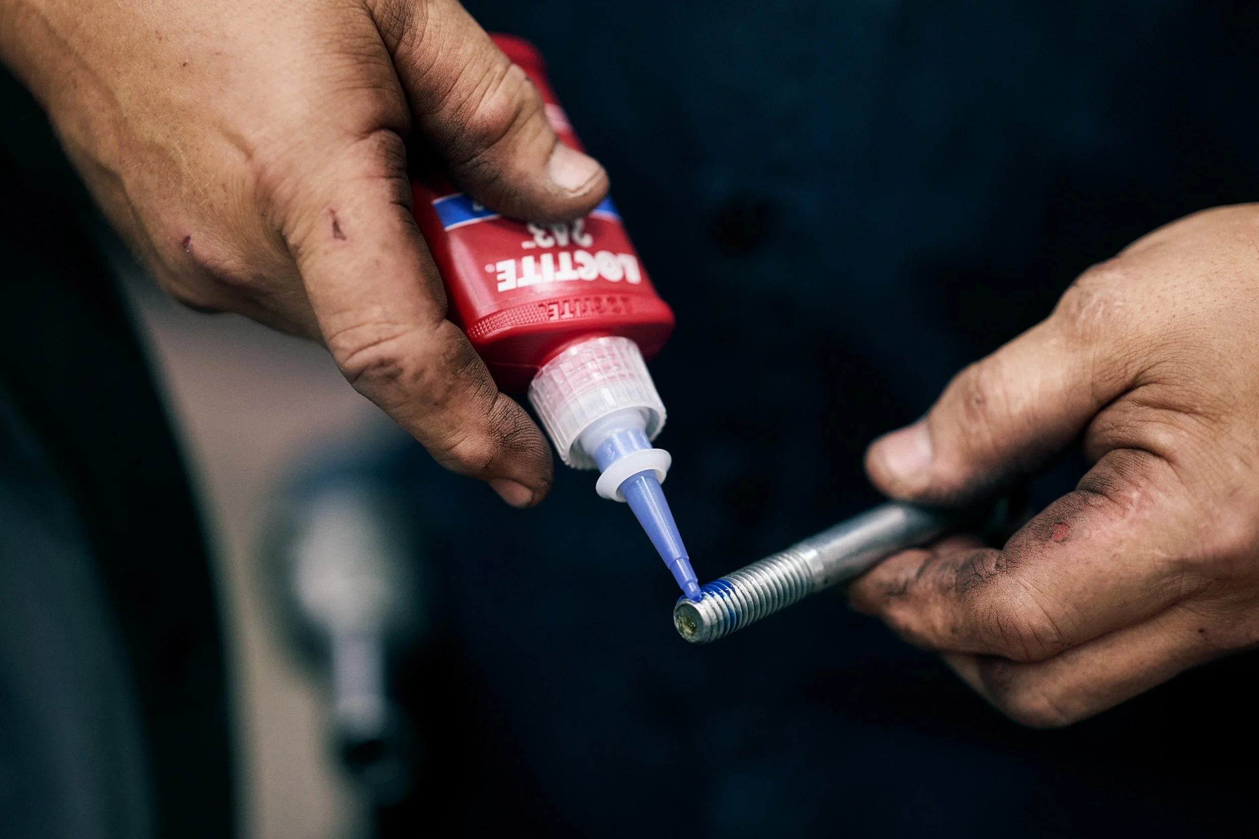 Hands applying LOCTITE adhesive to threaded bolt in workshop