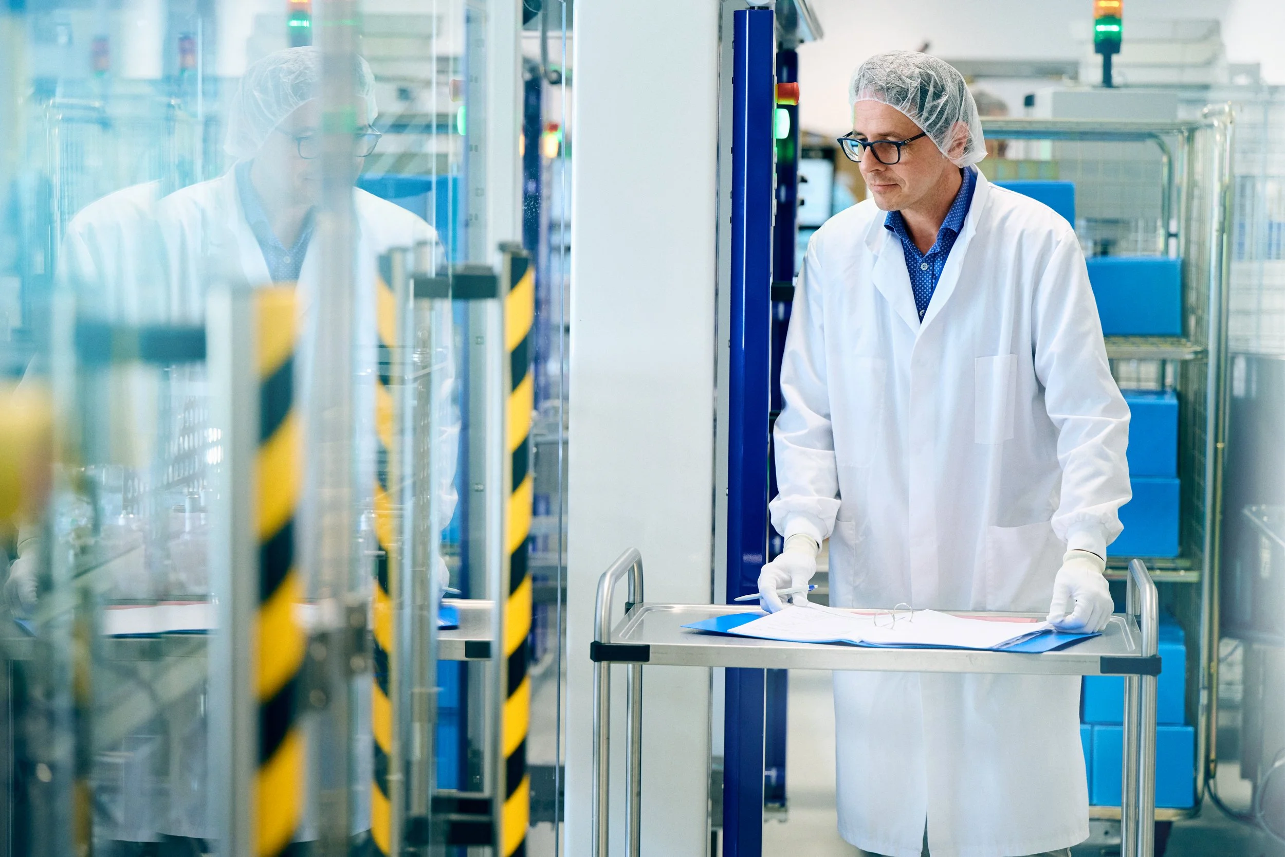 Technician monitoring process through glass barrier in controlled laboratory or production line
