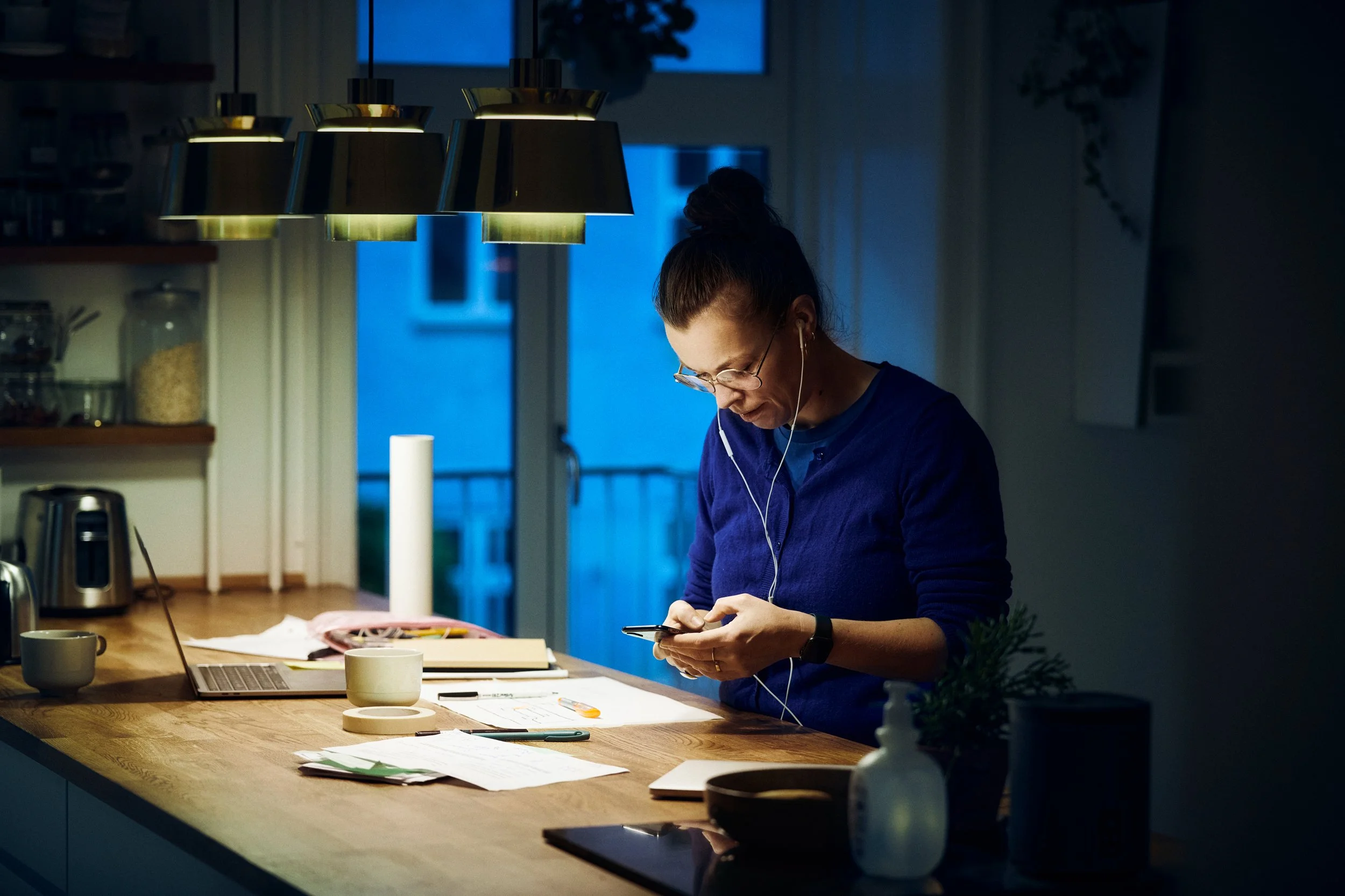 Woman working at table with laptop and documents in home setting, evening work moment