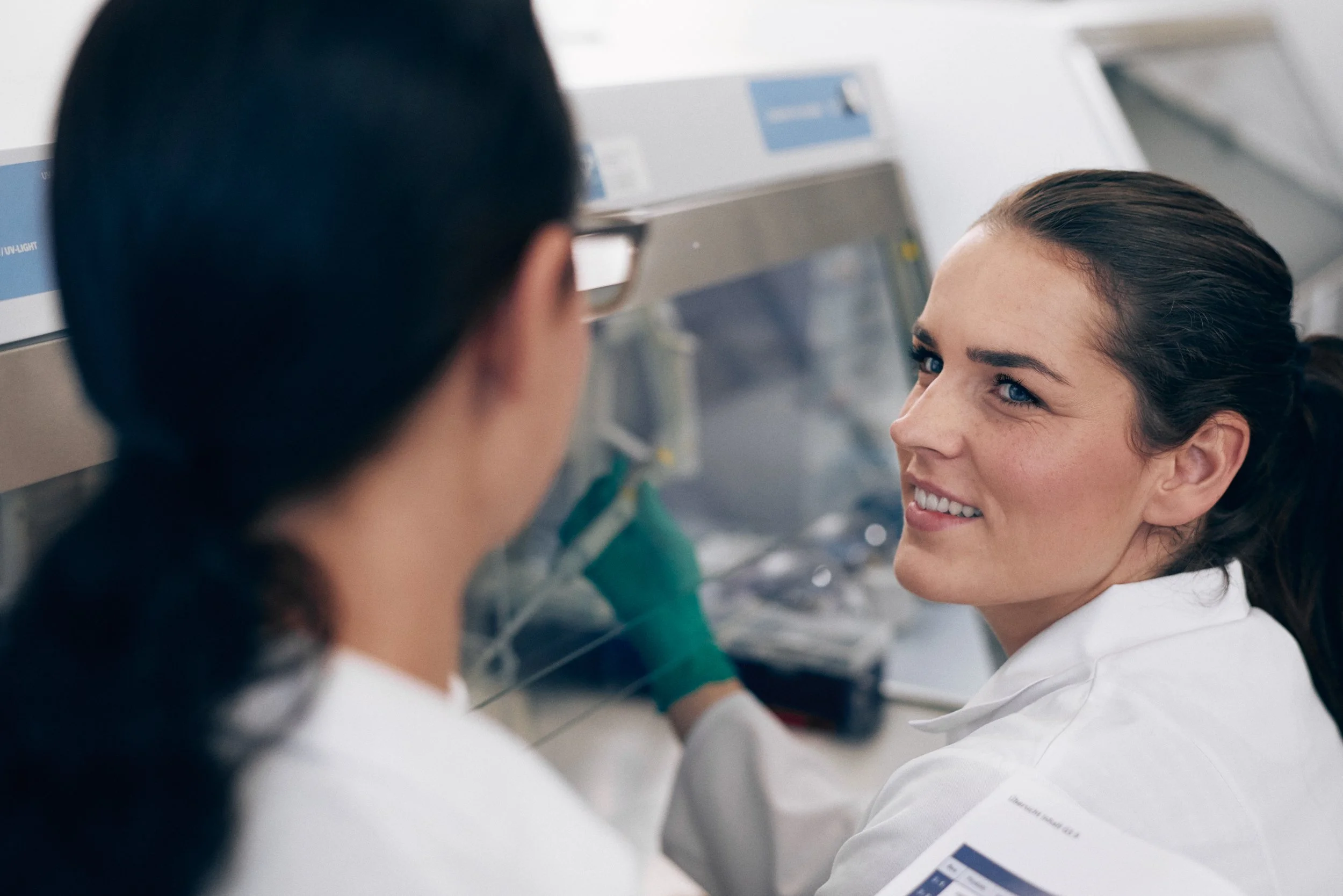Technician operating laboratory equipment while interacting with colleague, active collaboration