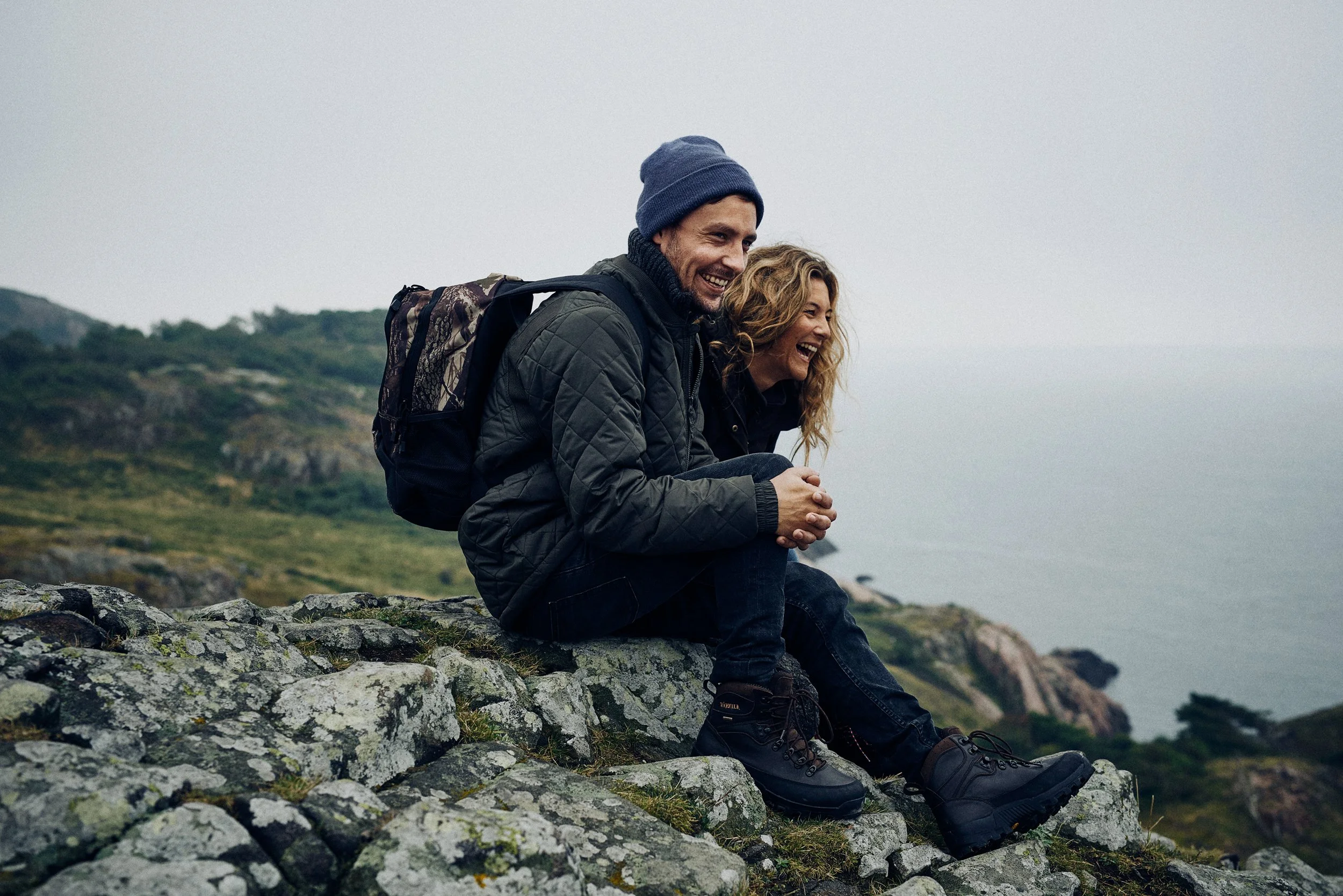 Couple sitting on rocky coastline smiling together, relaxed outdoor moment