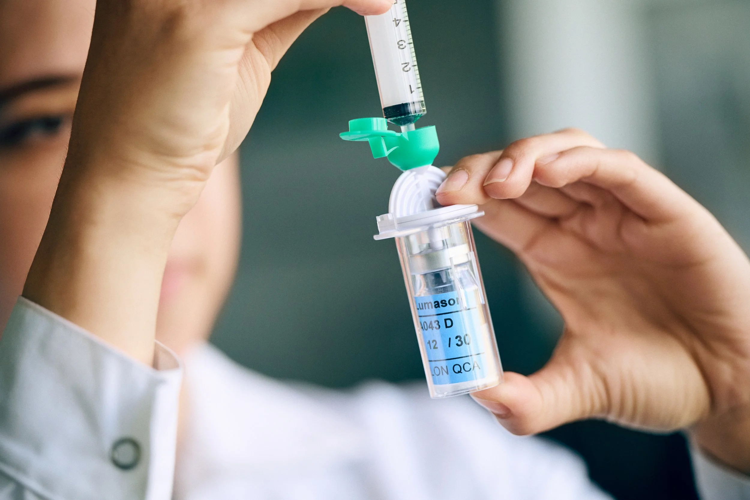 Technician transferring liquid into sample container using syringe, controlled dosing process