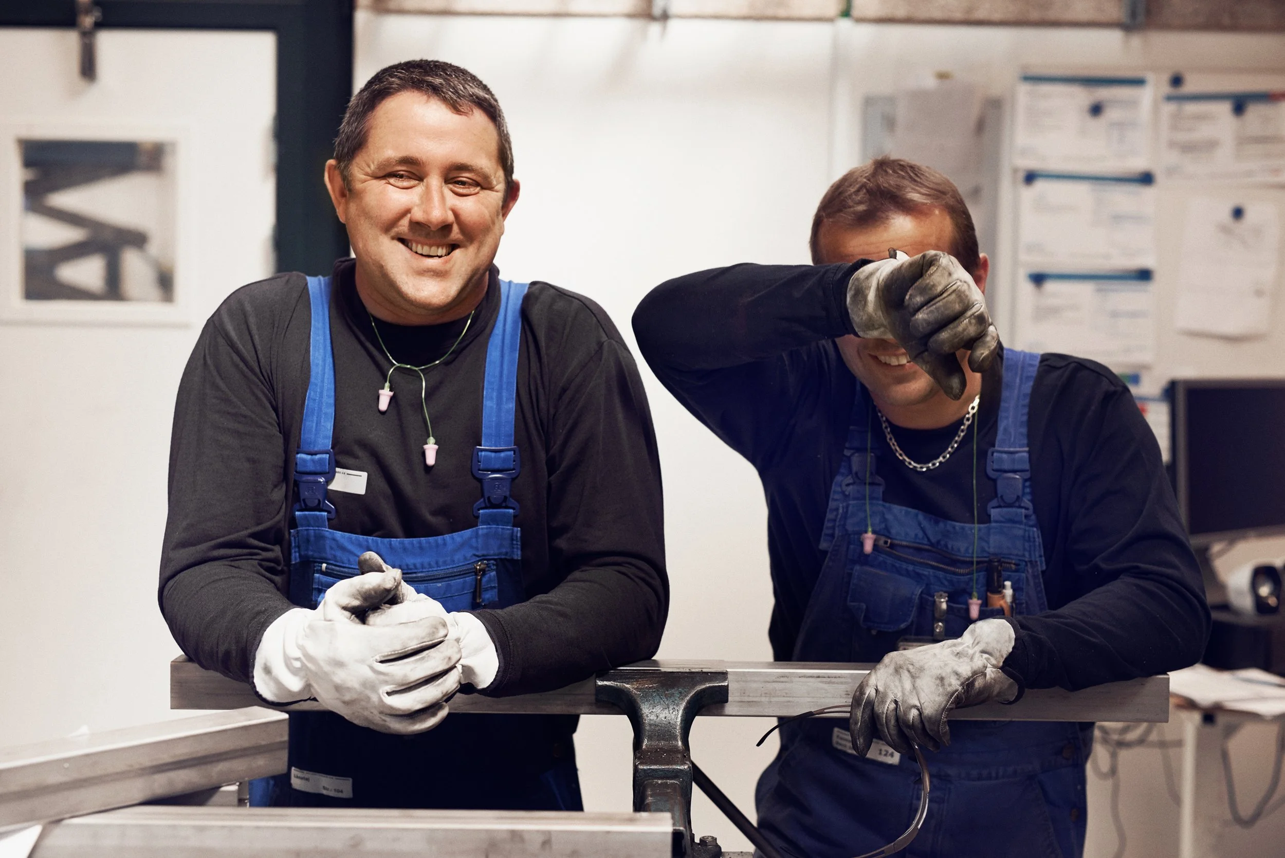 Two technicians wearing work gloves and overalls standing by metal workbench in workshop