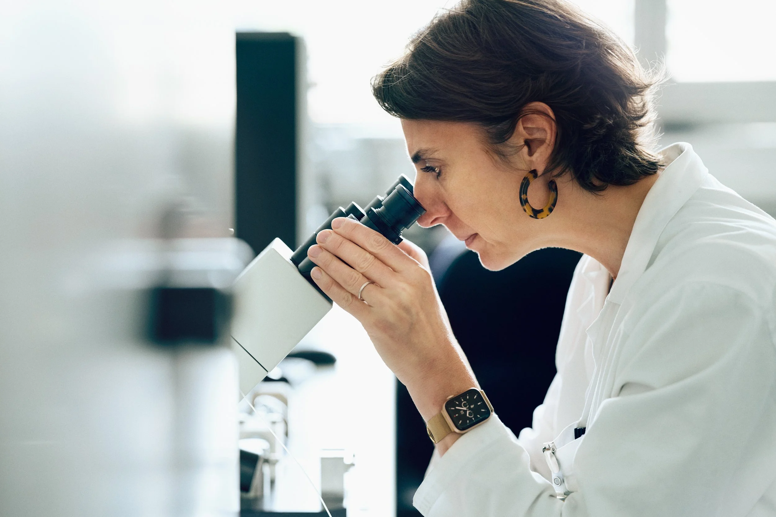 Scientist using microscope for material or compound analysis in controlled setting
